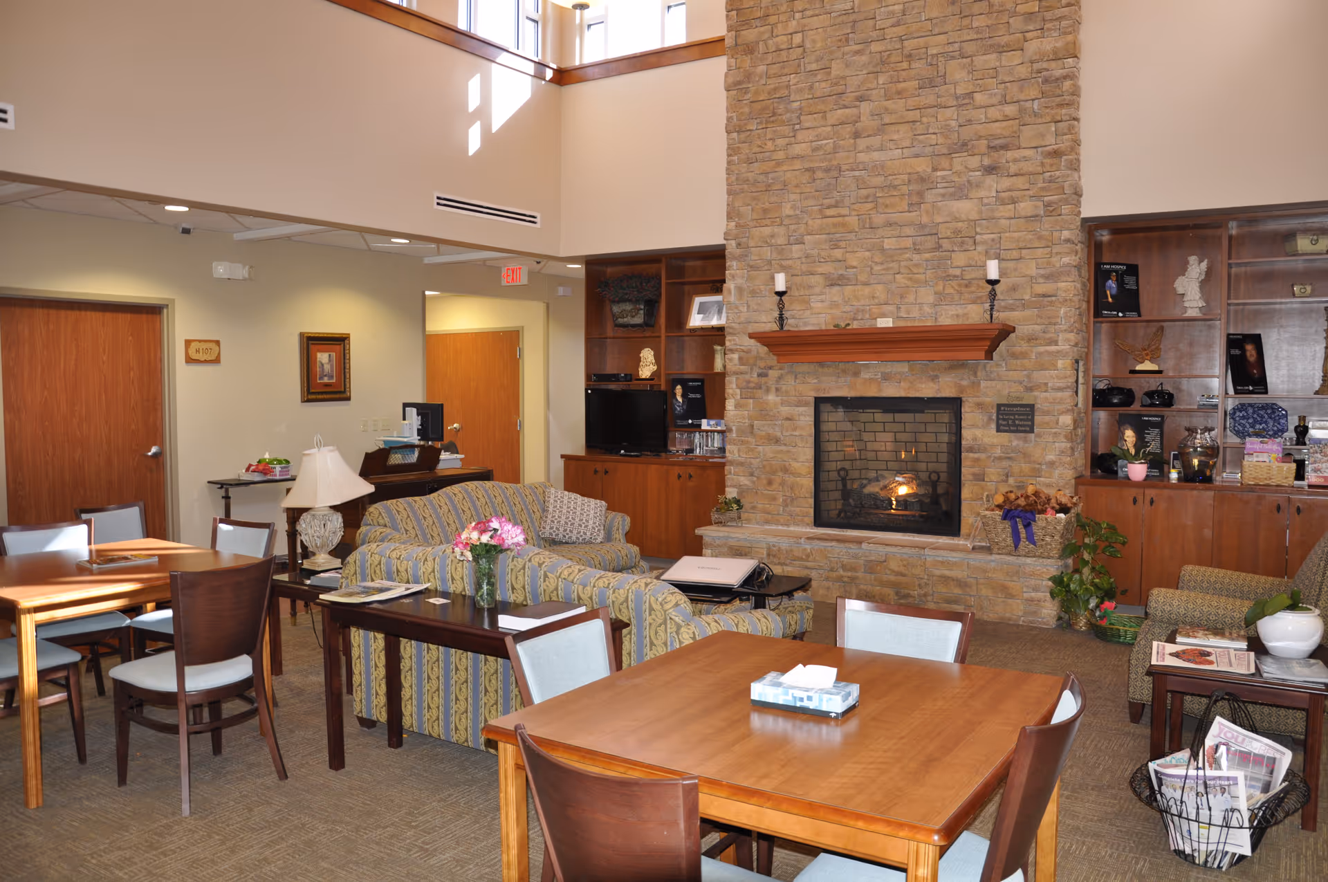 Cozy senior living lounge with a stone fireplace, couches, and wooden tables.