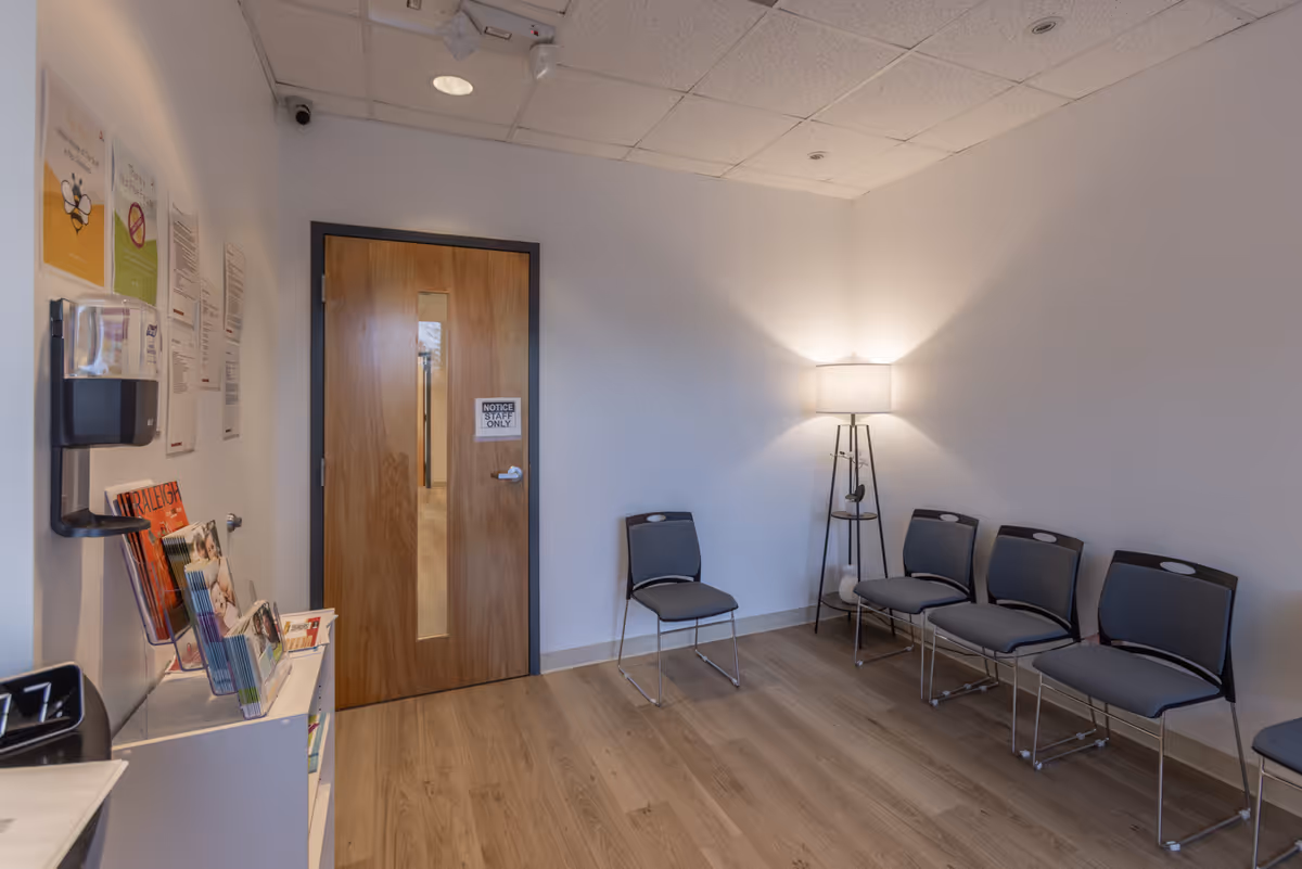 A quiet interior waiting area with gray chairs, magazines, a floor lamp, and a wooden door.