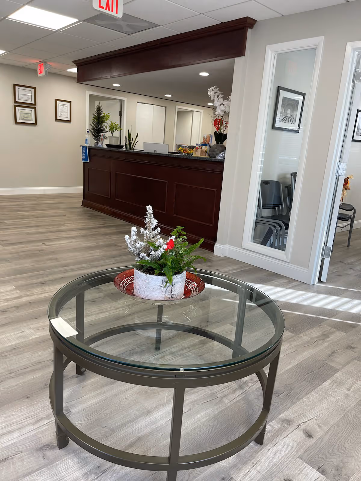 Lobby reception area with a dark wood counter, glass round table, and decorative planter.