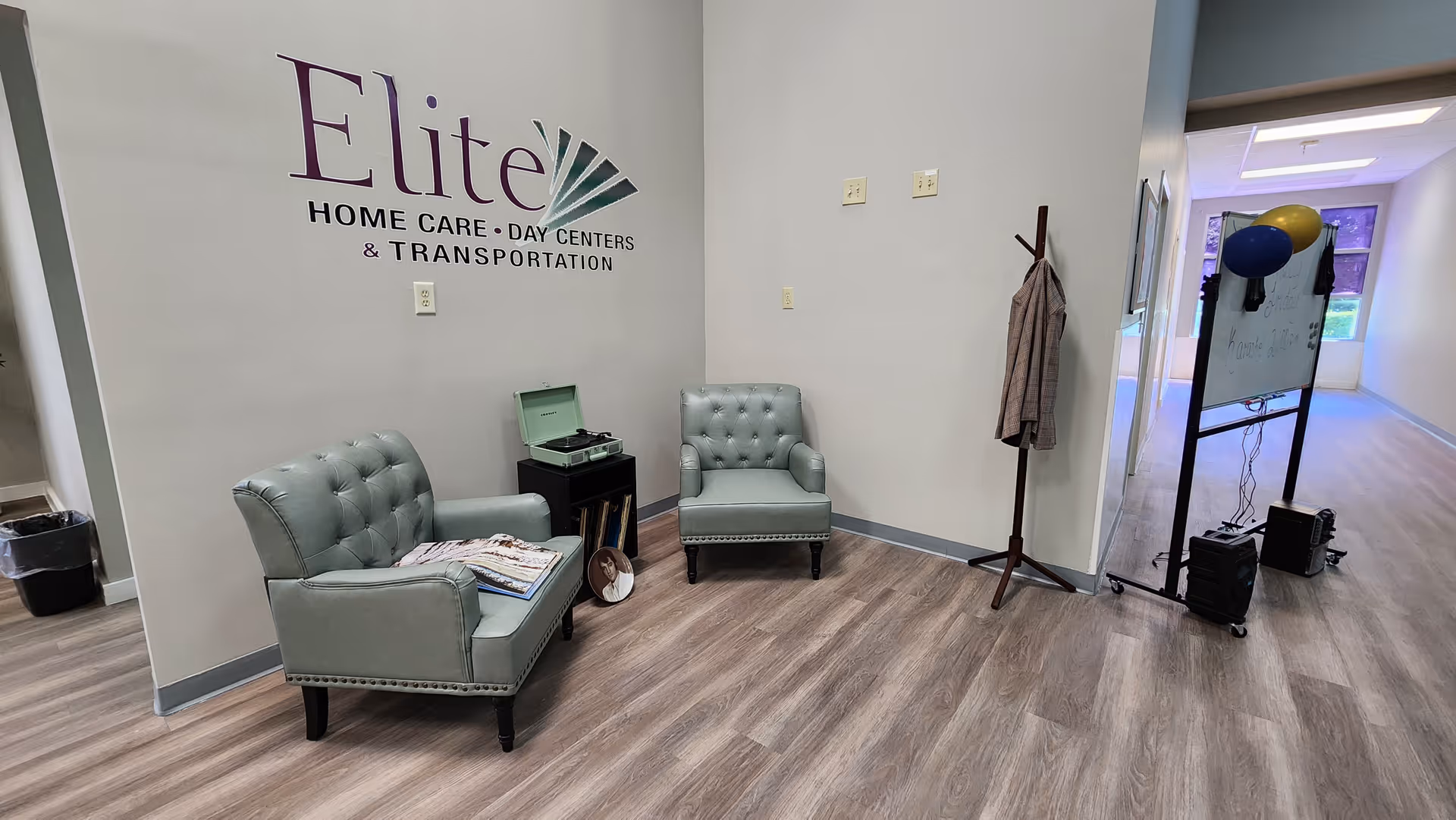 Lobby seating area with two teal tufted chairs, wall logo, and hallway with balloons.
