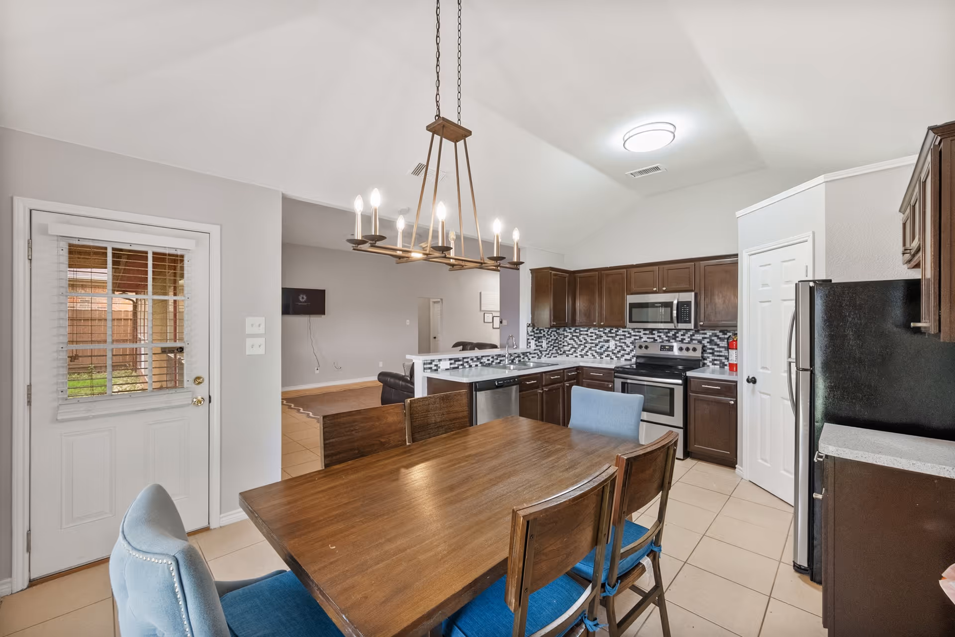 Open kitchen and dining area with wooden table, chandelier, and dark cabinetry.