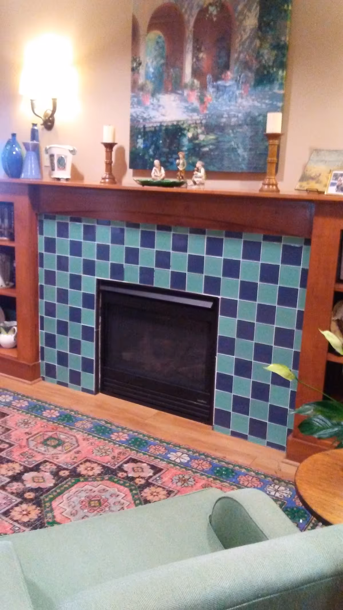 Cozy living room with a tiled fireplace, mantle decor, and a green sofa.