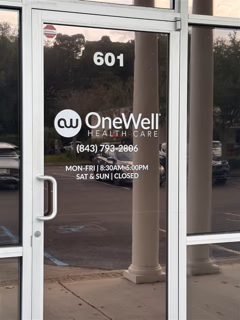 Glass entrance door shows OneWell Health Care logo, hours, and address 601.