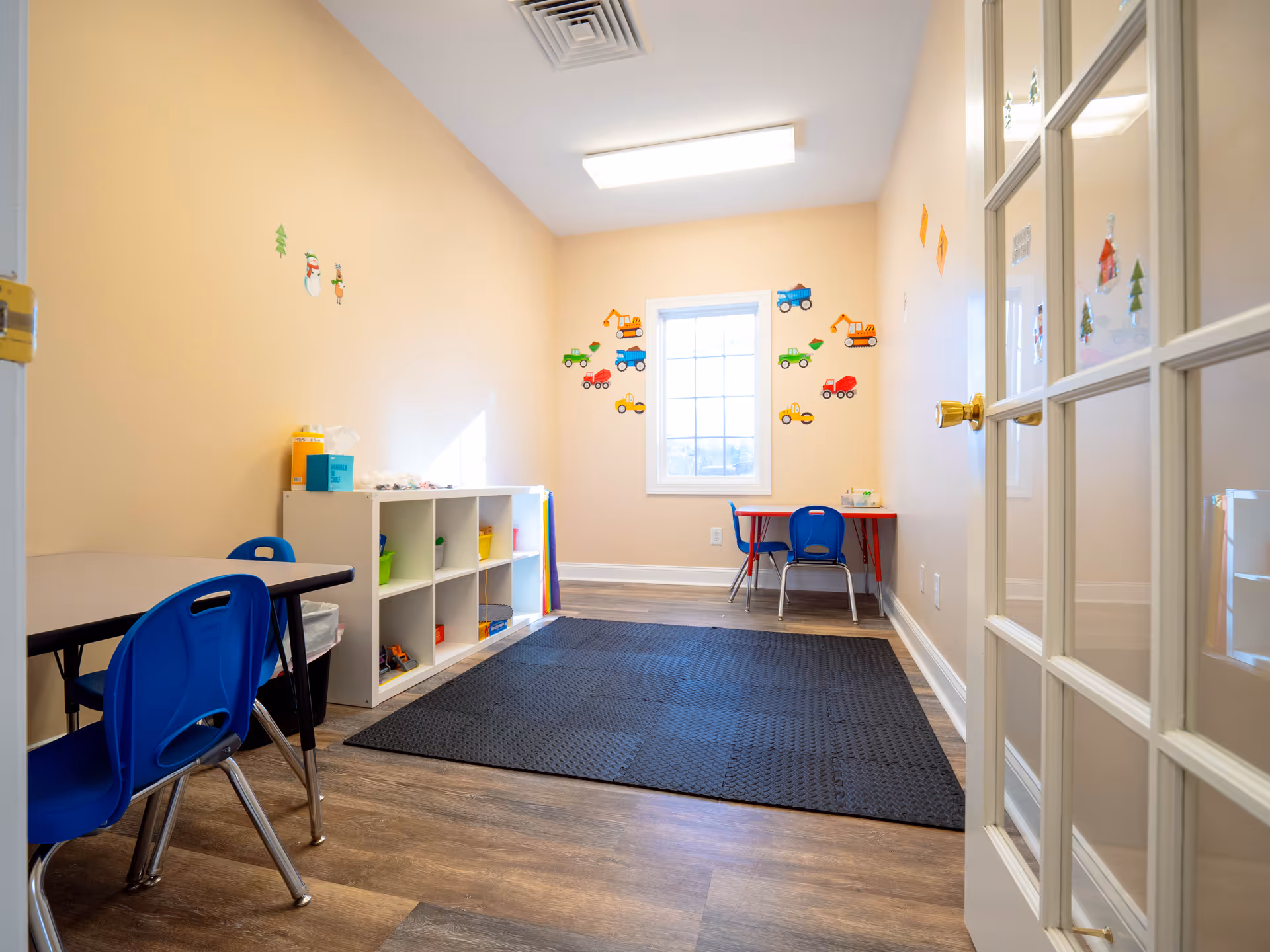 An interior activity room with blue chairs, cubbies, wall decals, and a dark rug.