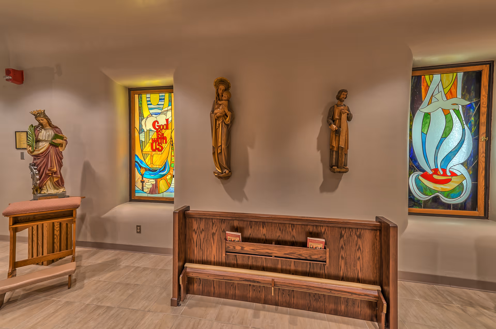 Interior chapel-like room with statues, pew bench, and colorful stained-glass windows.