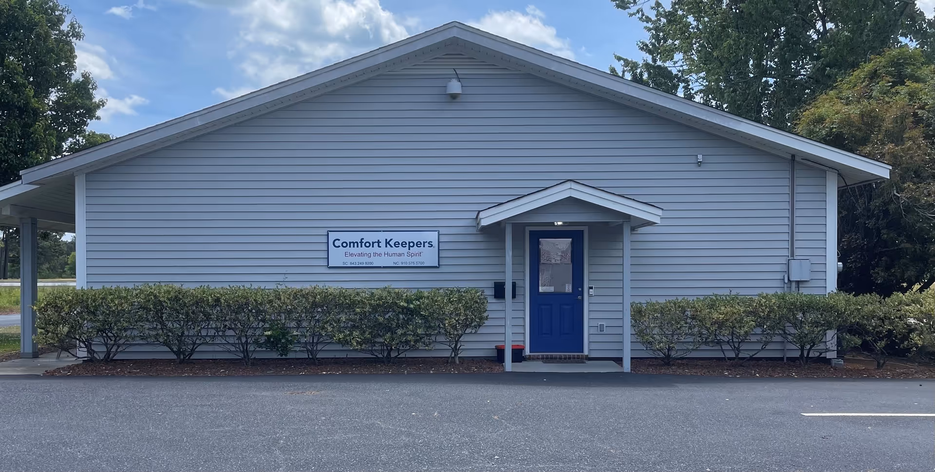 A single-story light-blue facility with a blue front door and trimmed hedges.