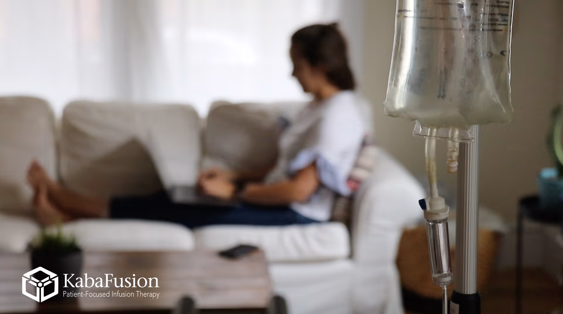 IV drip stand in foreground as a person relaxes on a white sofa nearby.