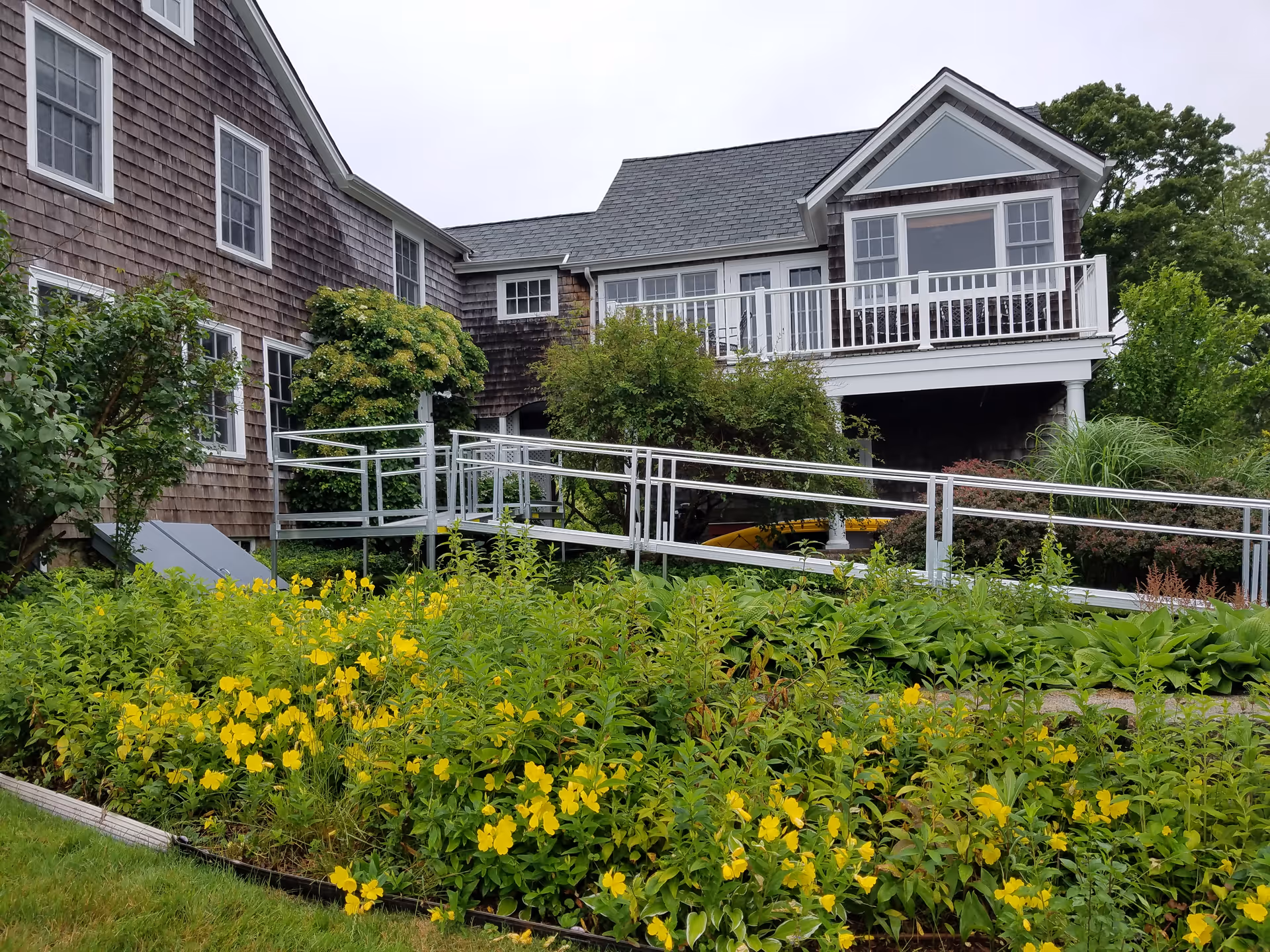 Exterior view of a senior living facility with wooden siding, ramp, and flowering garden.