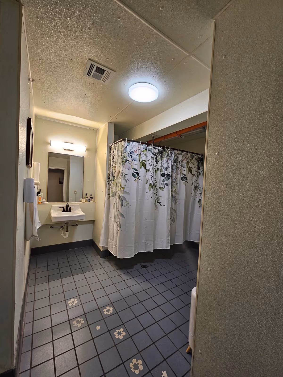 Interior bathroom with sink, mirror, floral shower curtain, and tiled floor.