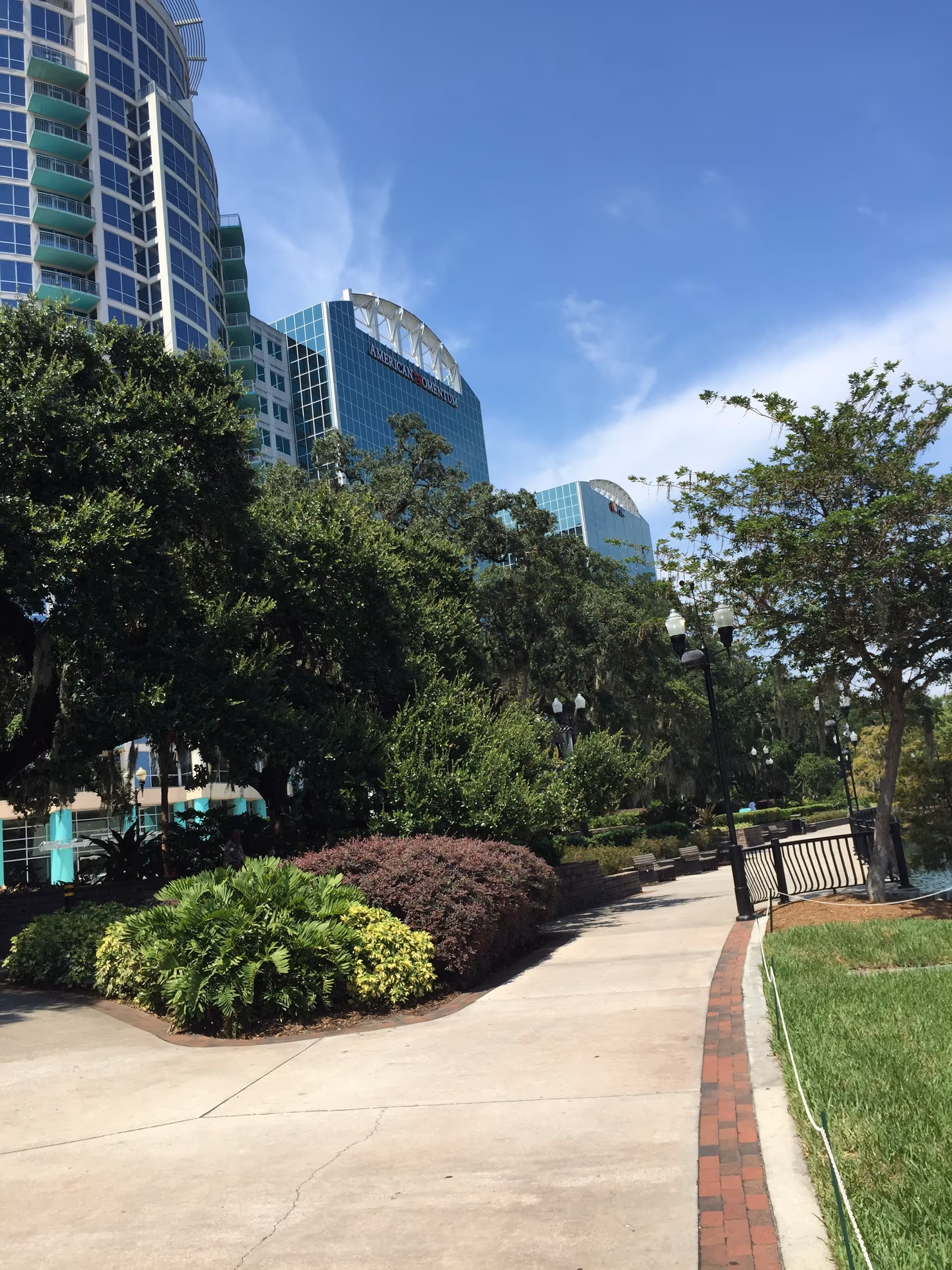 Sunny outdoor walkway with lush landscaping and modern high-rise buildings in the background