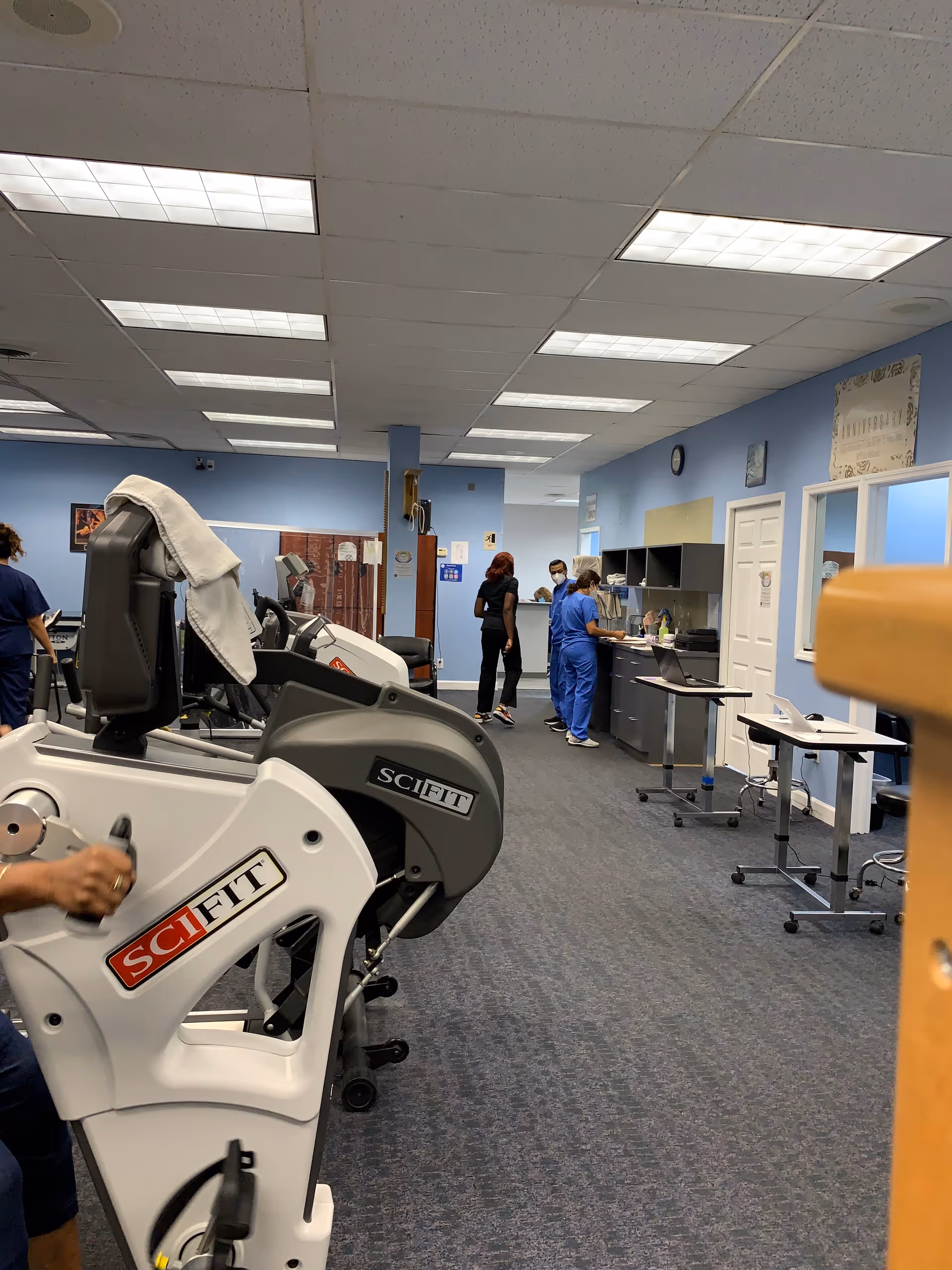 Therapy room with SCIFIT exercise machines, blue walls, and staff nearby.
