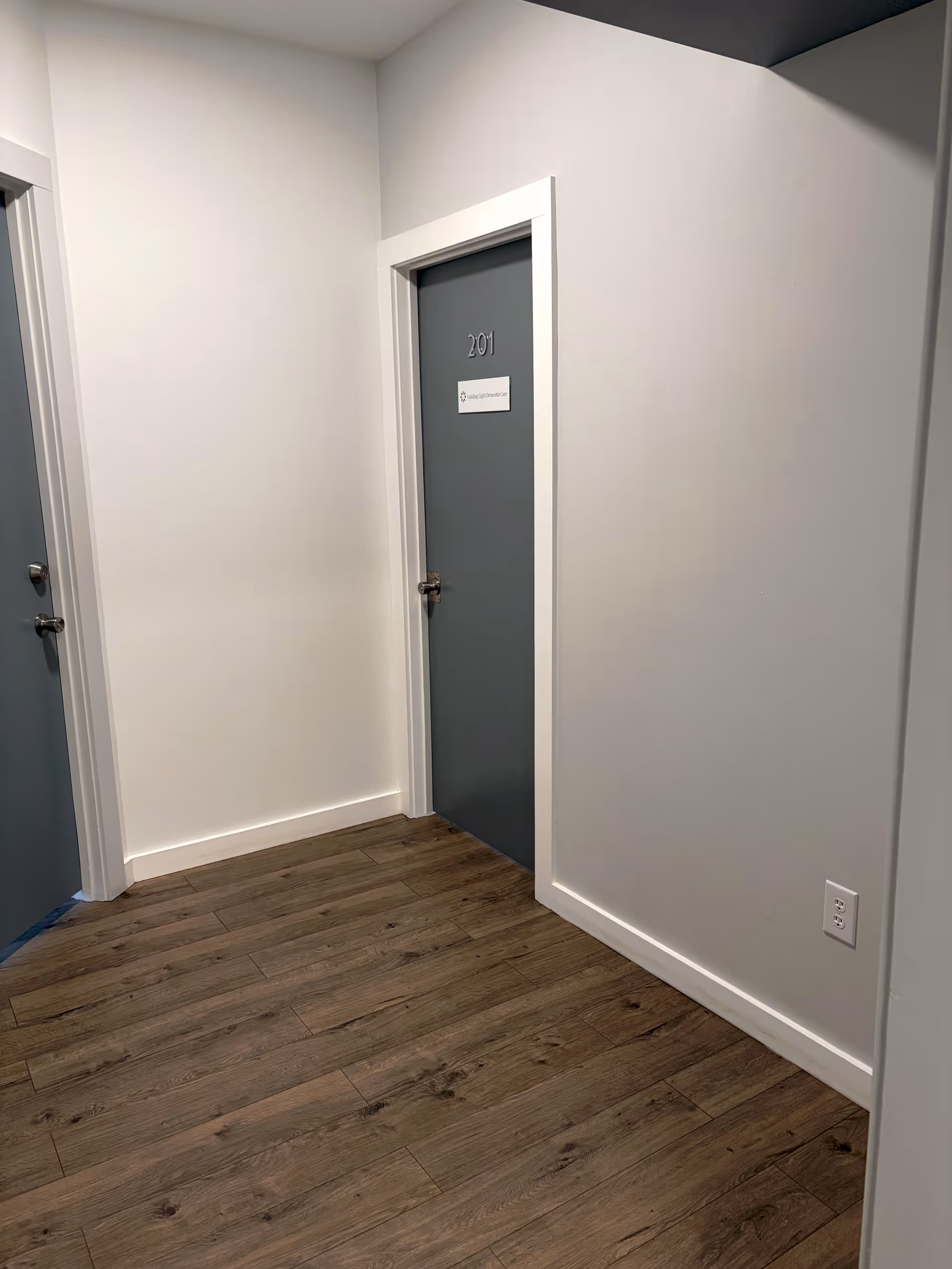 Narrow interior hallway of a senior living facility with blue doors and wood flooring.