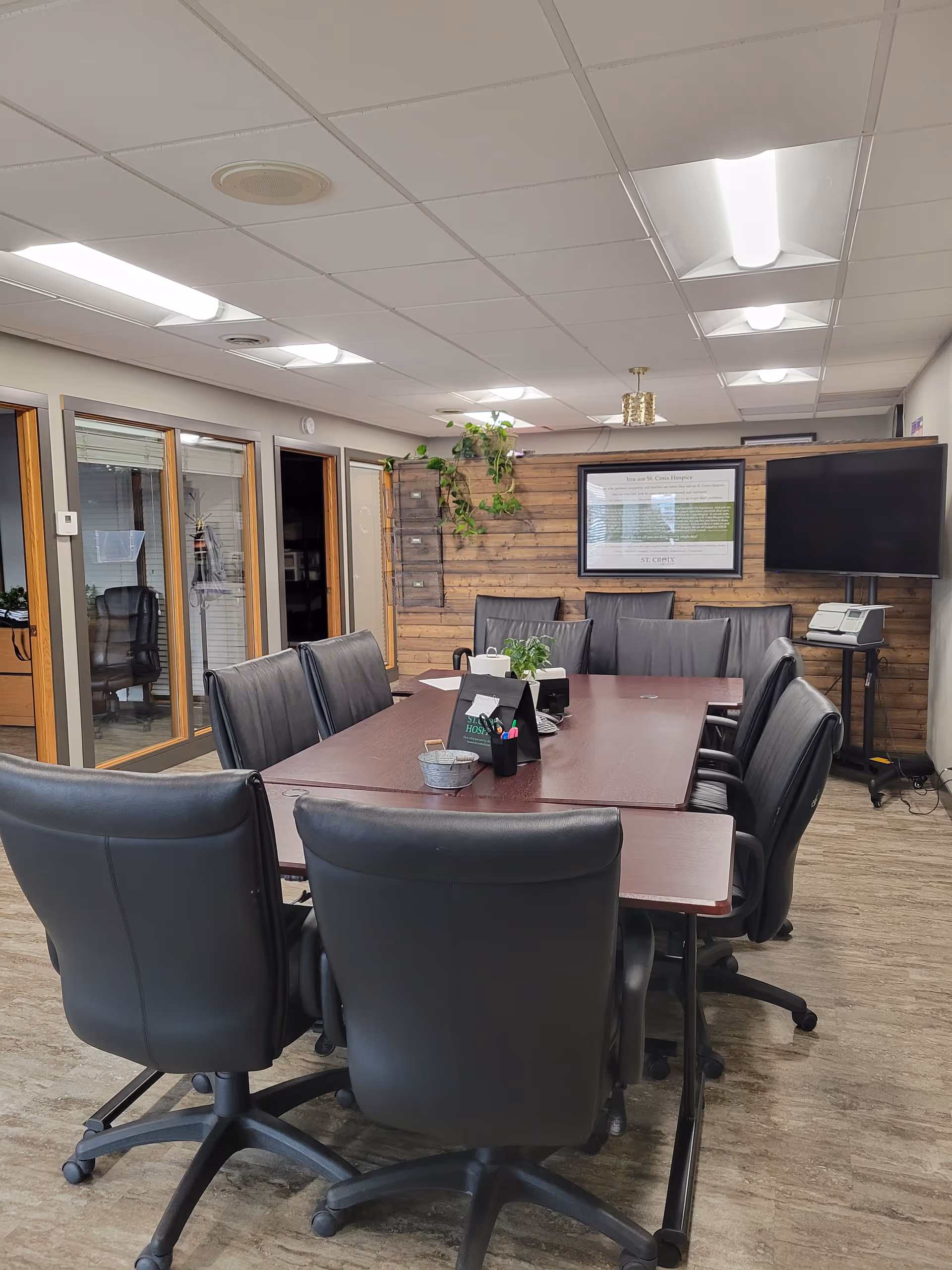 St. Croix Hospice conference room with a long table, black chairs, plants, and framed wall display.