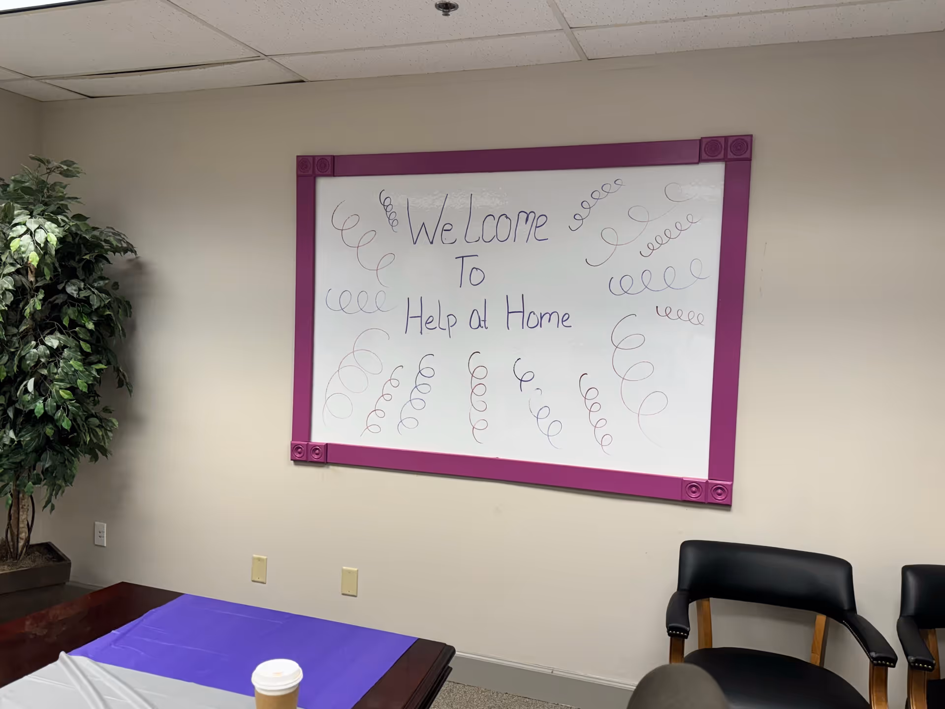 Interior room with a purple-framed welcome board reading Help at Home and chairs