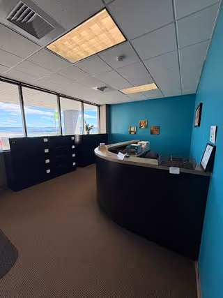Curved black reception desk in a teal-walled interior lobby of a senior care facility.