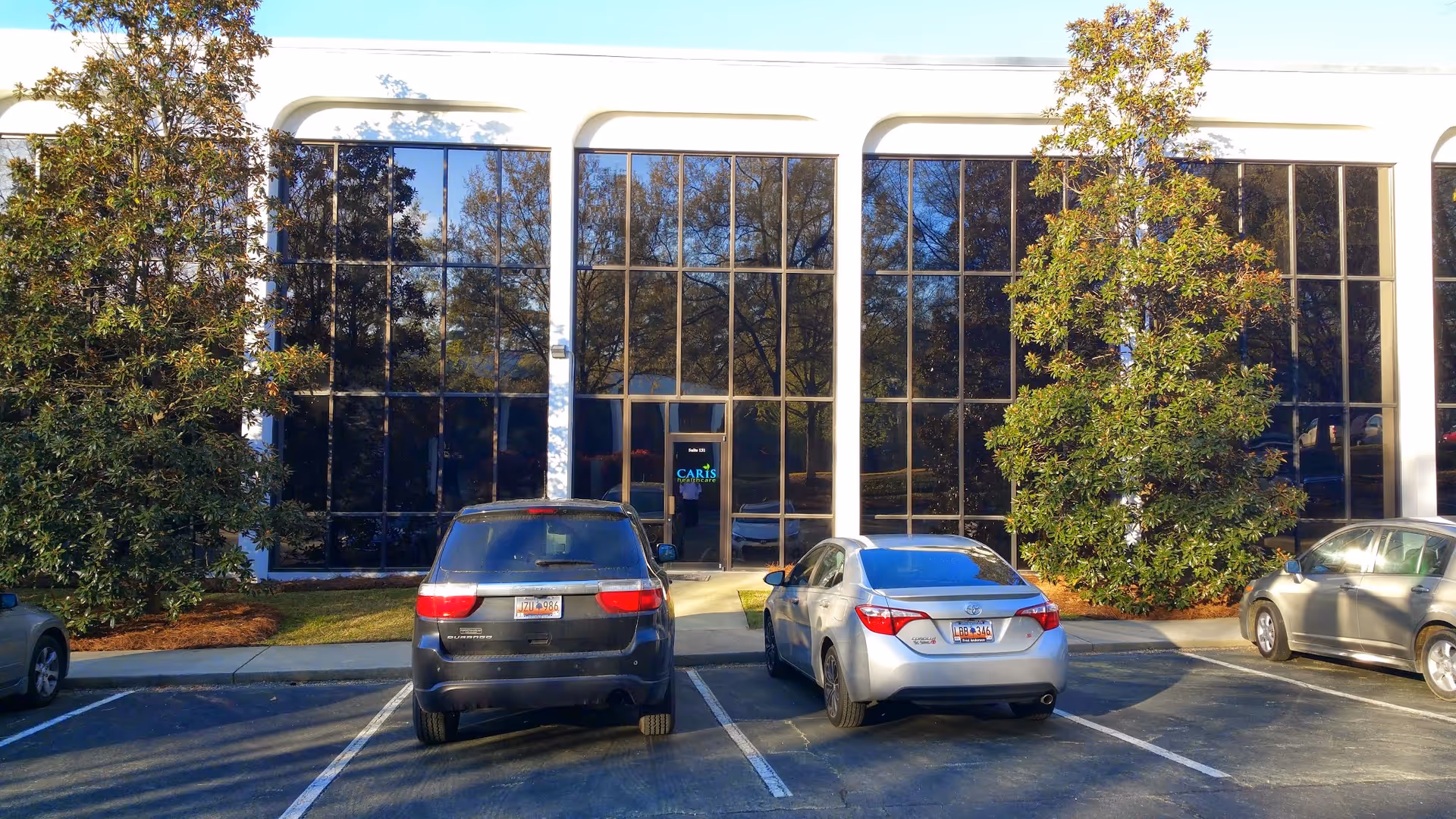 Caris Healthcare entrance with glass facade and parked cars in front.
