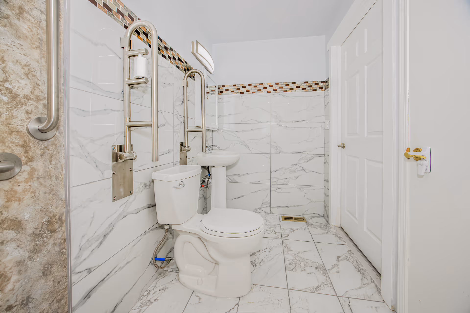 Clean bathroom featuring a toilet, pedestal sink, and wall-mounted safety grab bars.