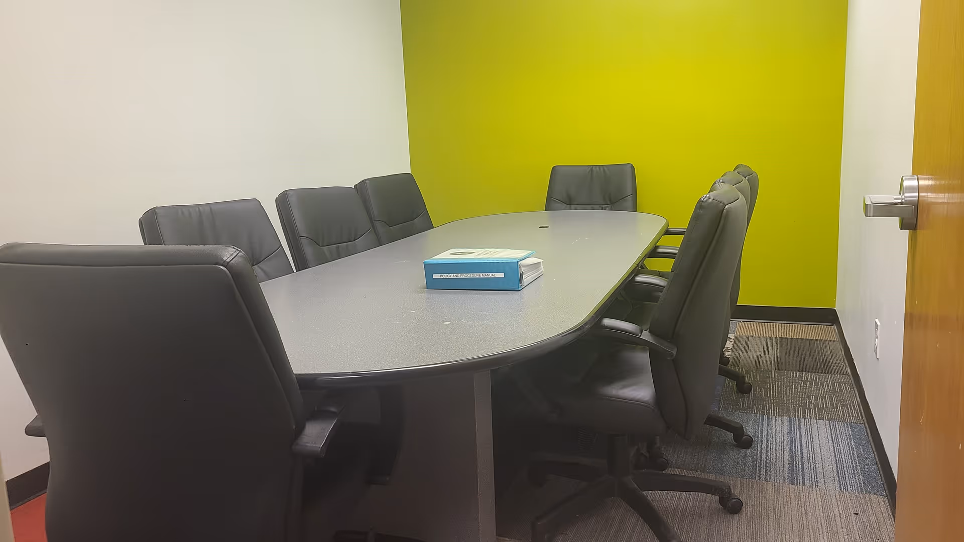 An oval conference table with black chairs in a lime-green meeting room.