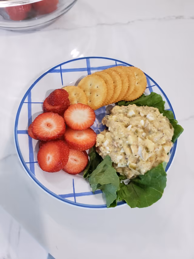 Plate with strawberries, crackers, and chicken salad on greens on a white table.