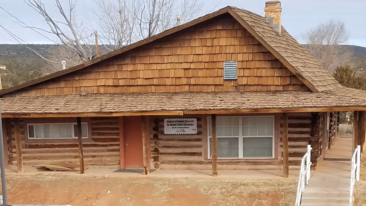 Rustic log cabin facility with a covered porch, red door, and front sign.