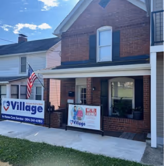 Brick senior care building with porch signs, an American flag, and a grassy front yard.