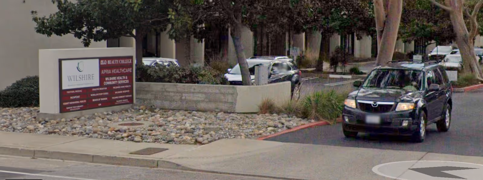 Exterior view of a facility entrance with a sign and a parked SUV.