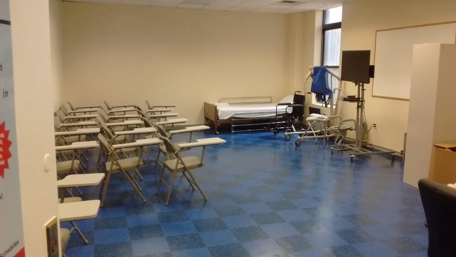 A clinical room with blue tiled floor, folding chairs, a hospital bed, and medical equipment.