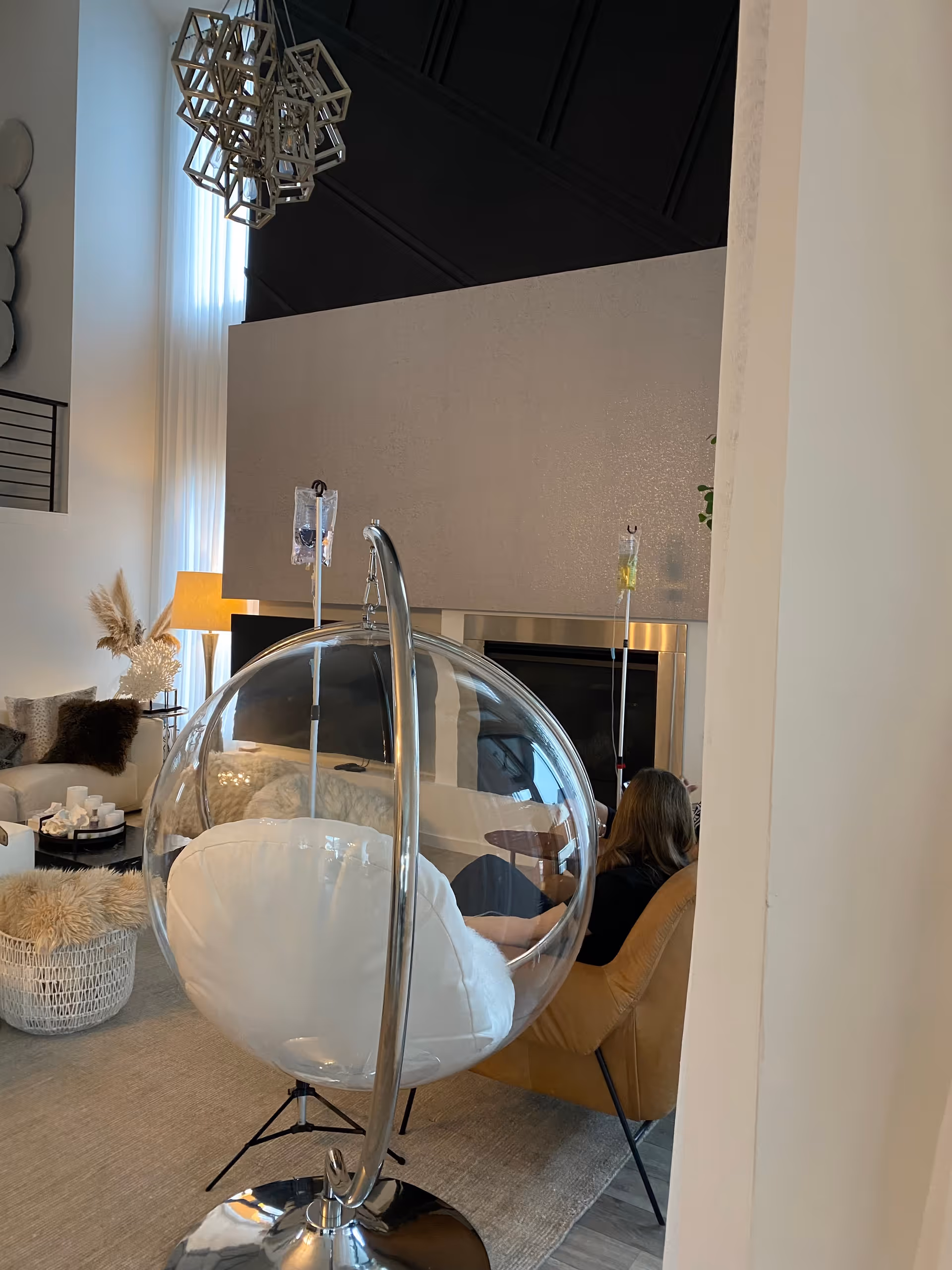 Modern living room with a clear glass bubble chair and a resident seated nearby.