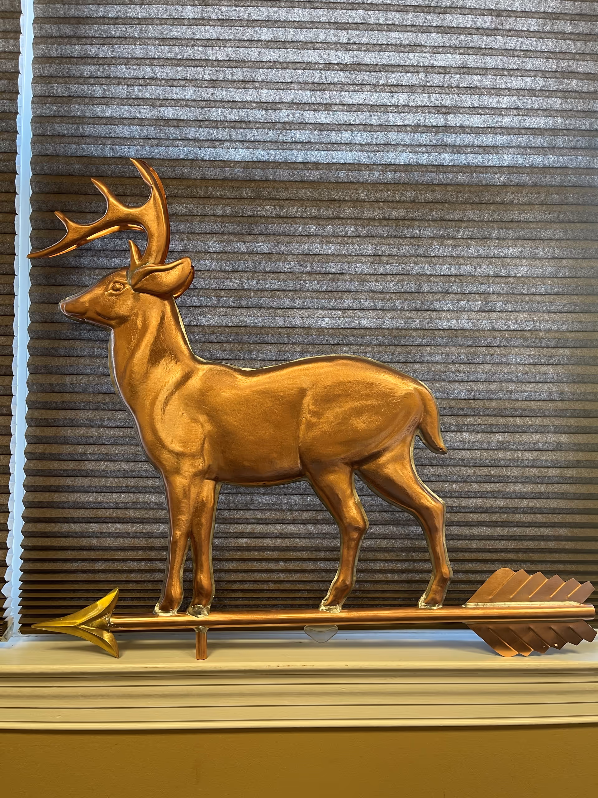 Golden deer statue with arrow decor sits by textured brown blinds.