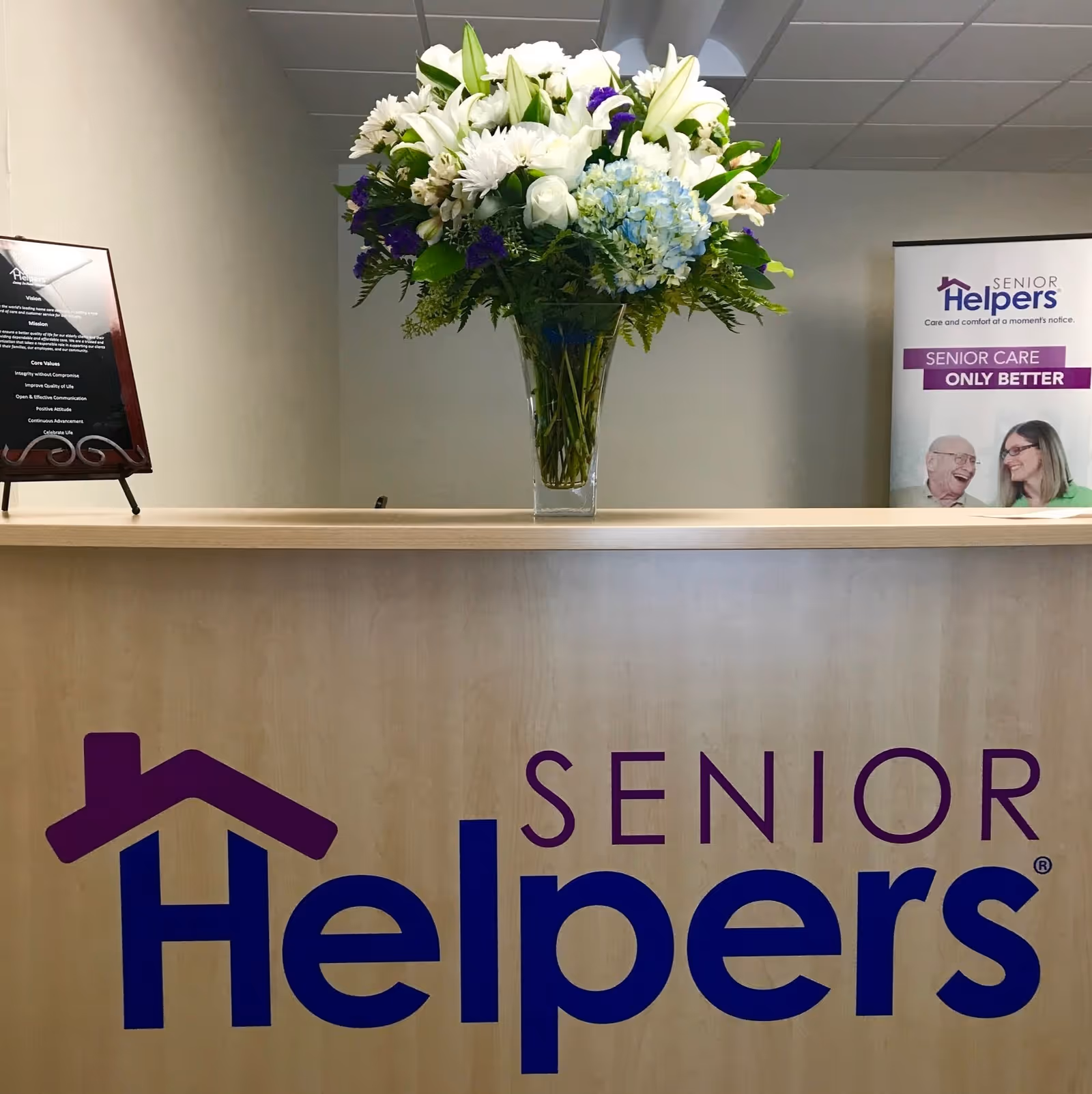 Reception desk with a large flower arrangement and a Senior Helpers banner.