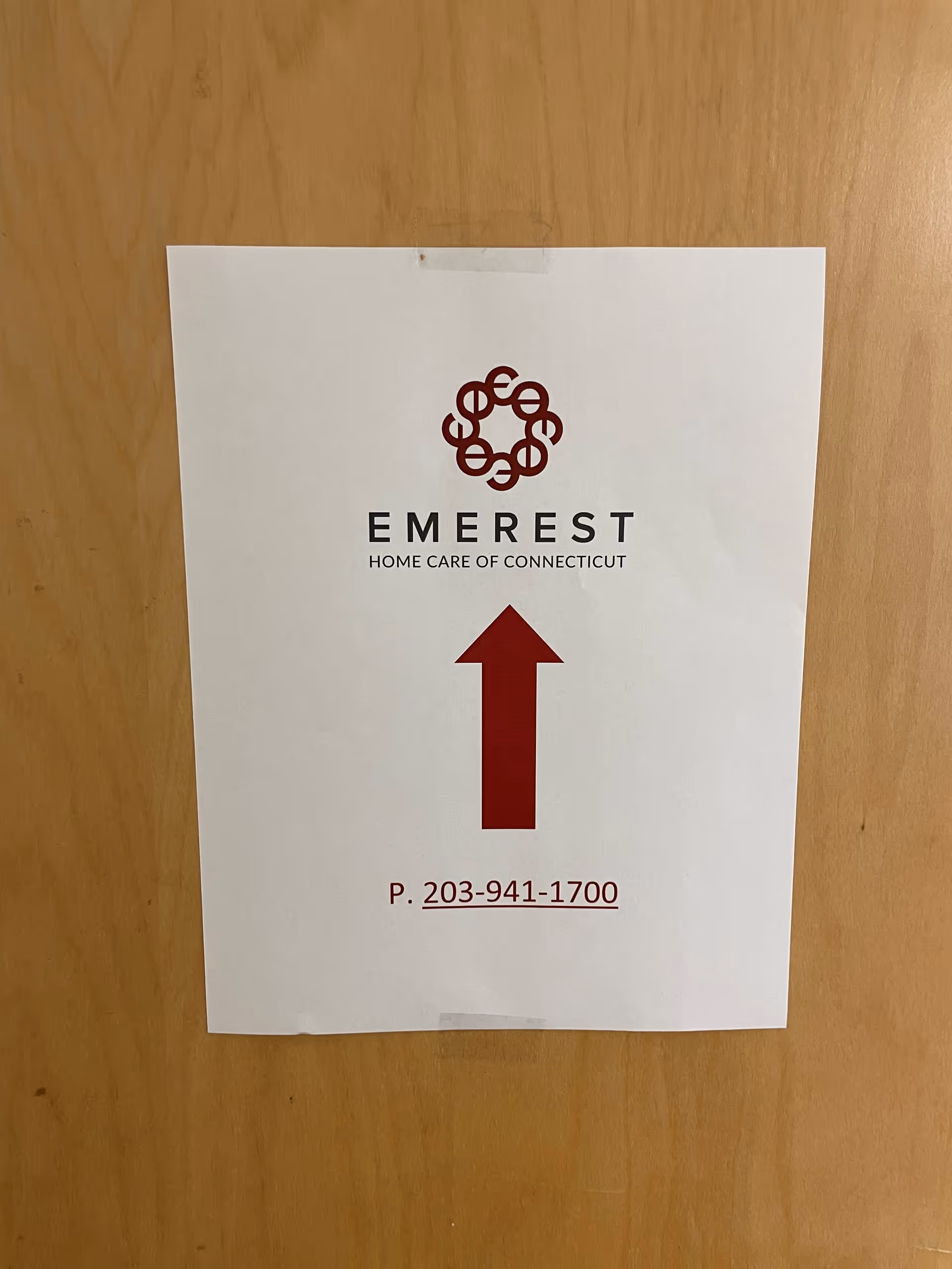 White sign on a wooden wall showing Emerest Home Care of Connecticut logo and arrow.