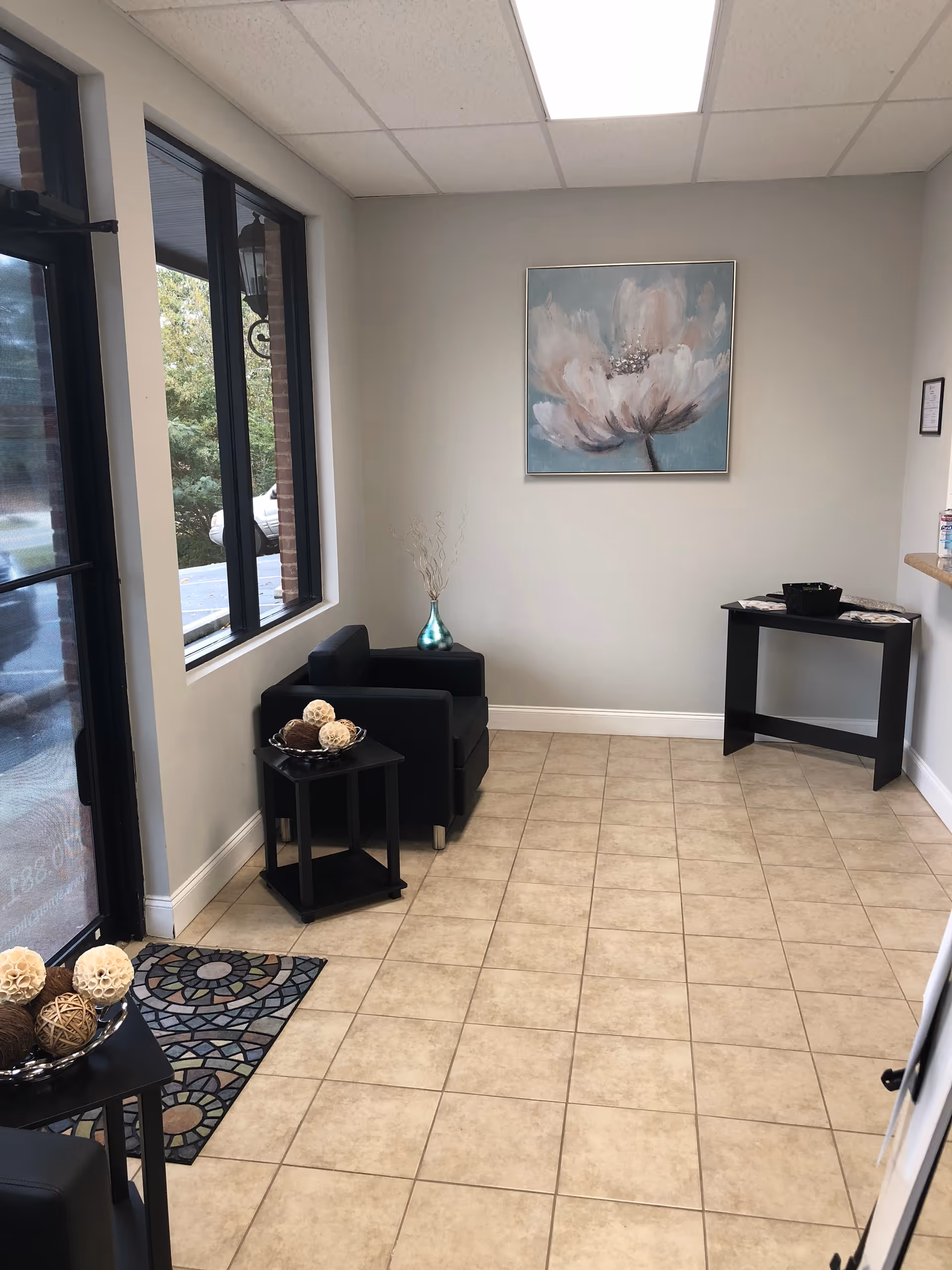 A clean modern lobby with black chairs, side tables, tiled floor, and abstract wall art.
