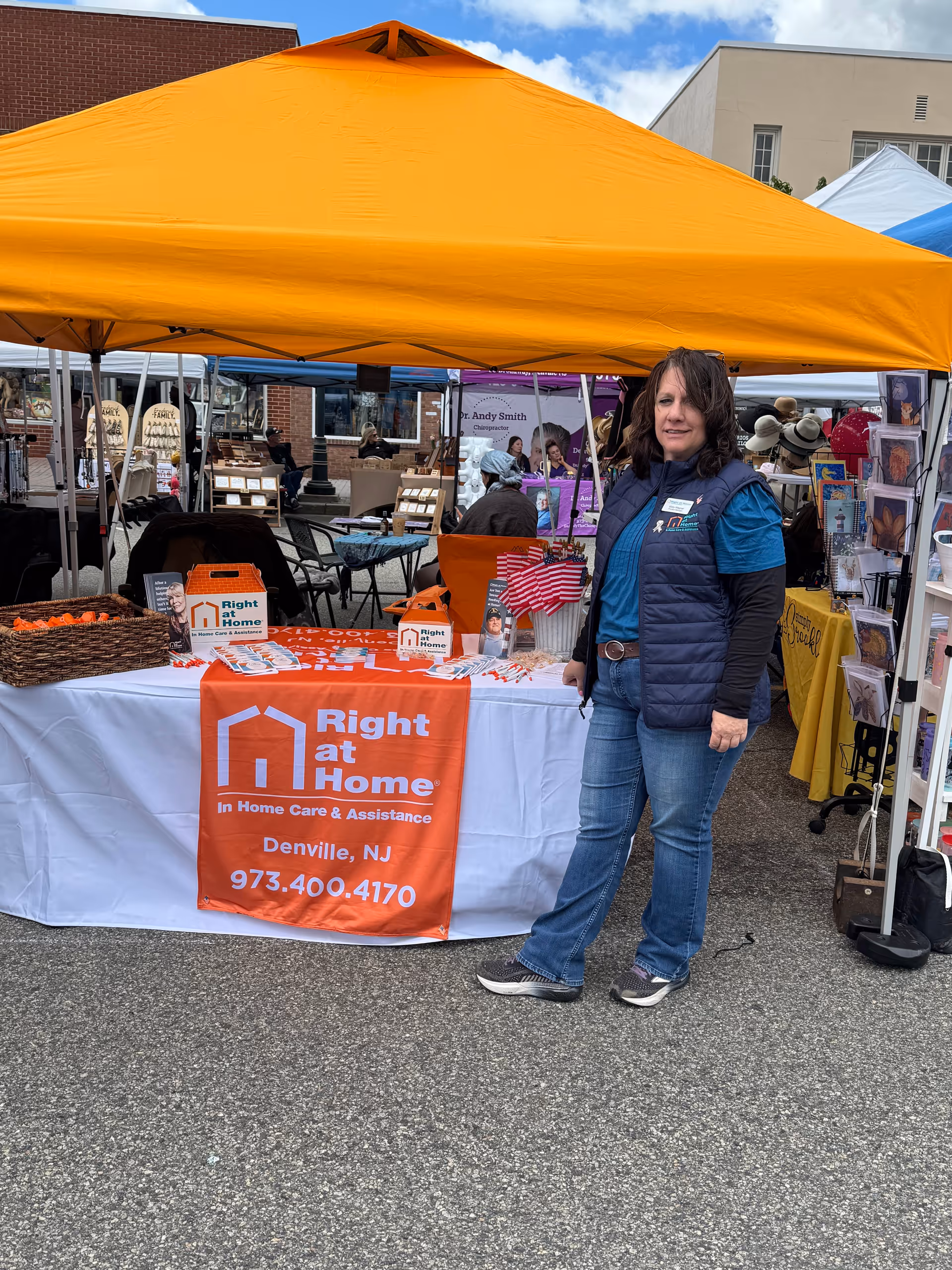 Right at Home booth under orange canopy at outdoor market with staff