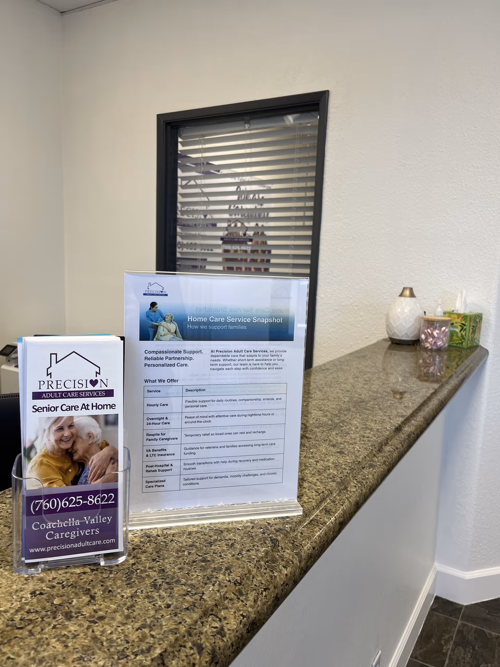 Reception counter with brochures on a granite surface near a window with blinds.