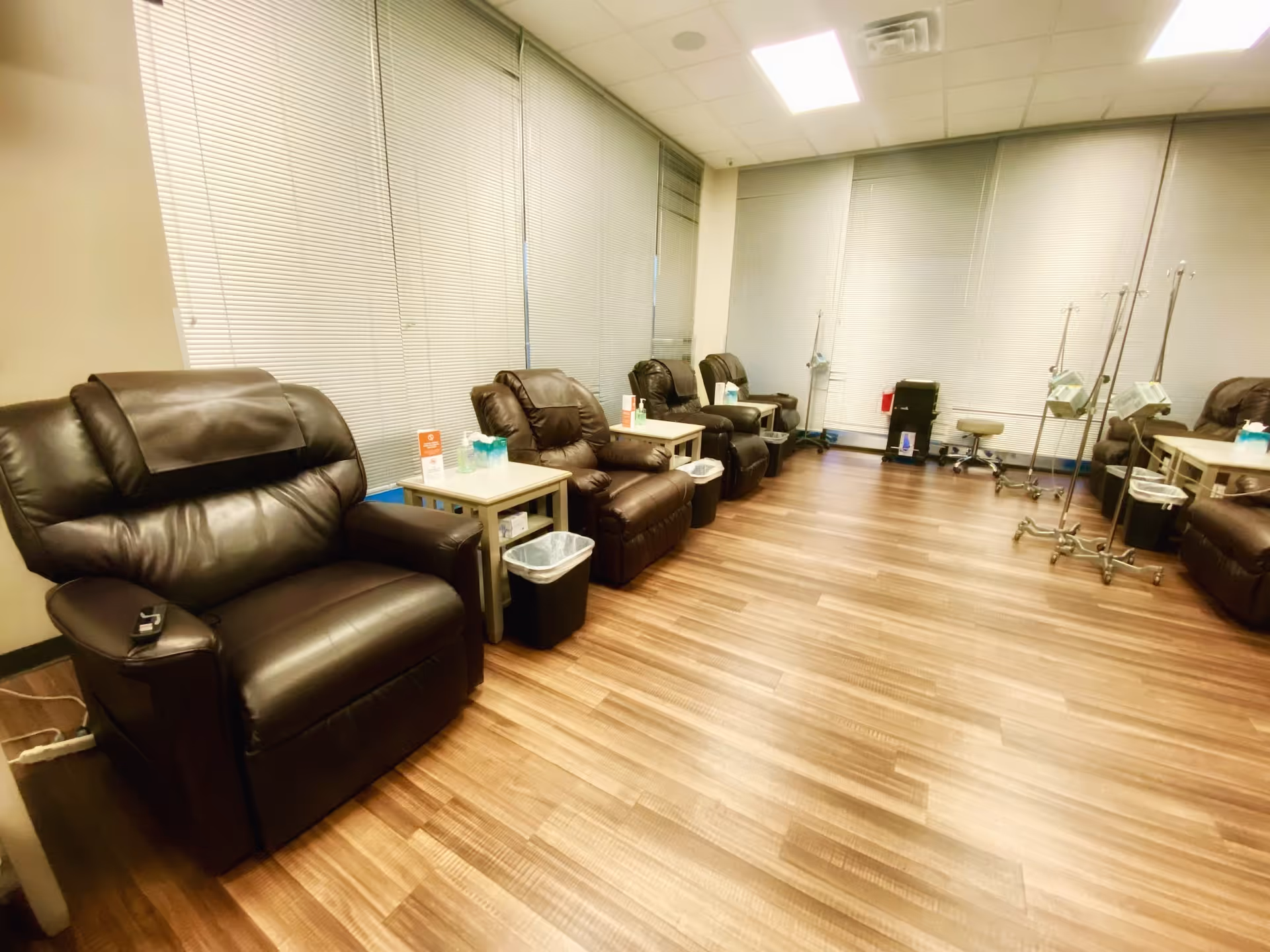 Infusion center lounge with brown leather chairs, small tables, and IV stands along windowed walls.