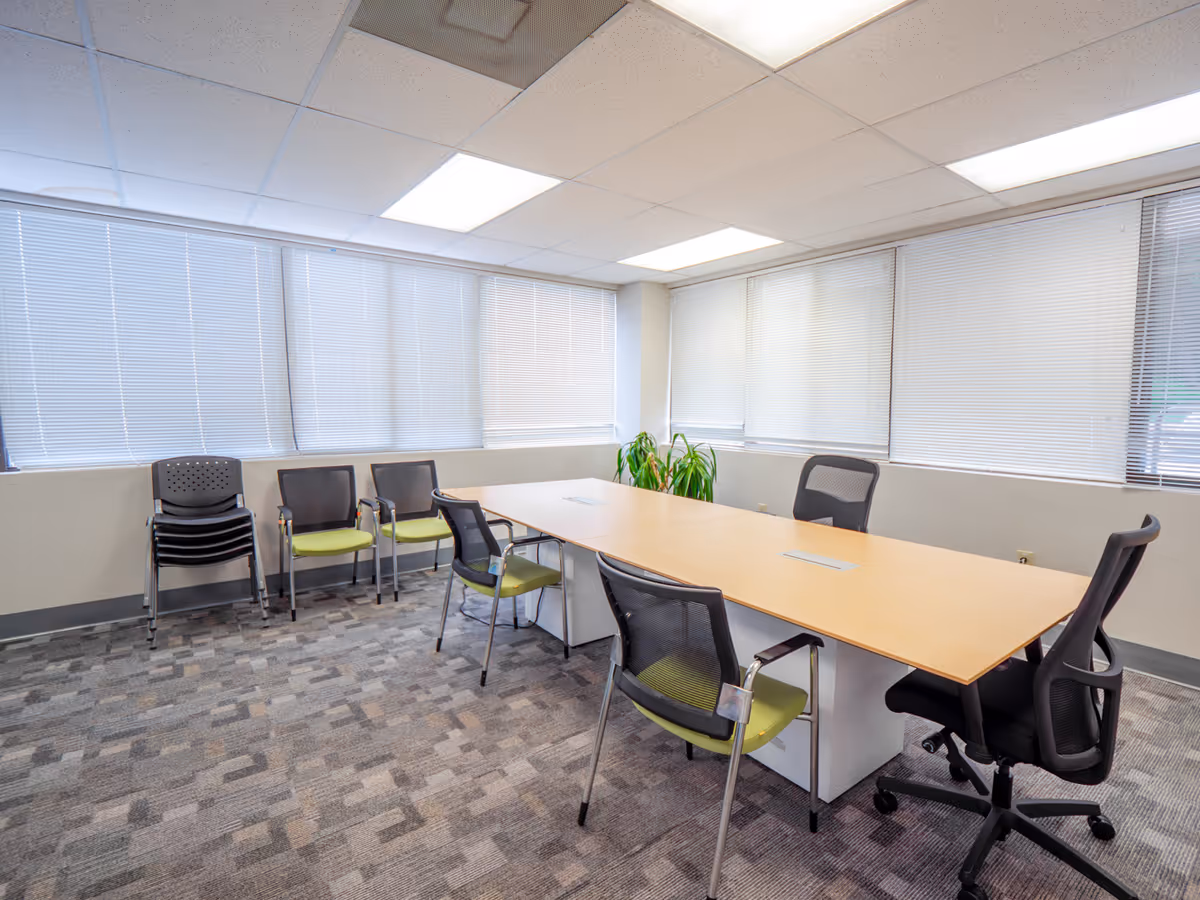 A conference room with a long table, multiple chairs, and windows with blinds.