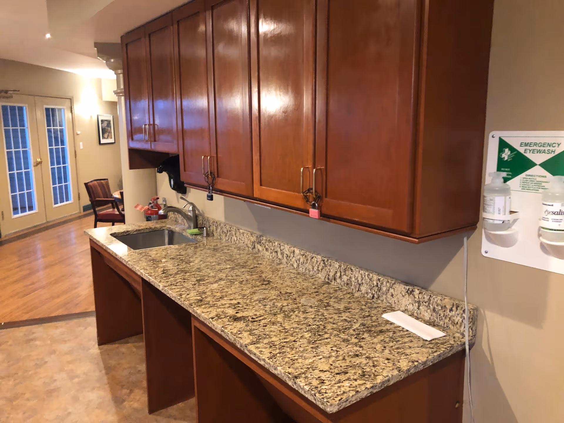 Wooden cabinets line a granite countertop kitchen with sink in a senior living facility.