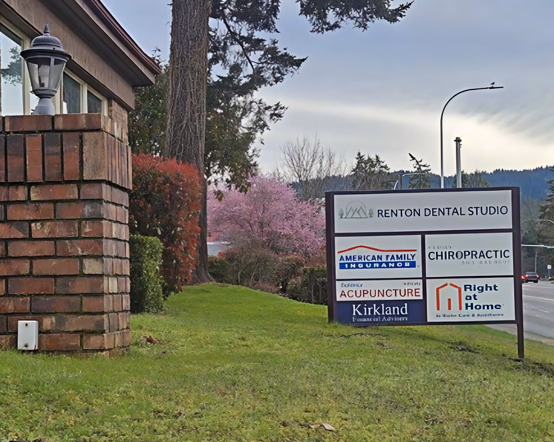 Outdoor signboard beside a brick building listing Right at Home and other businesses.