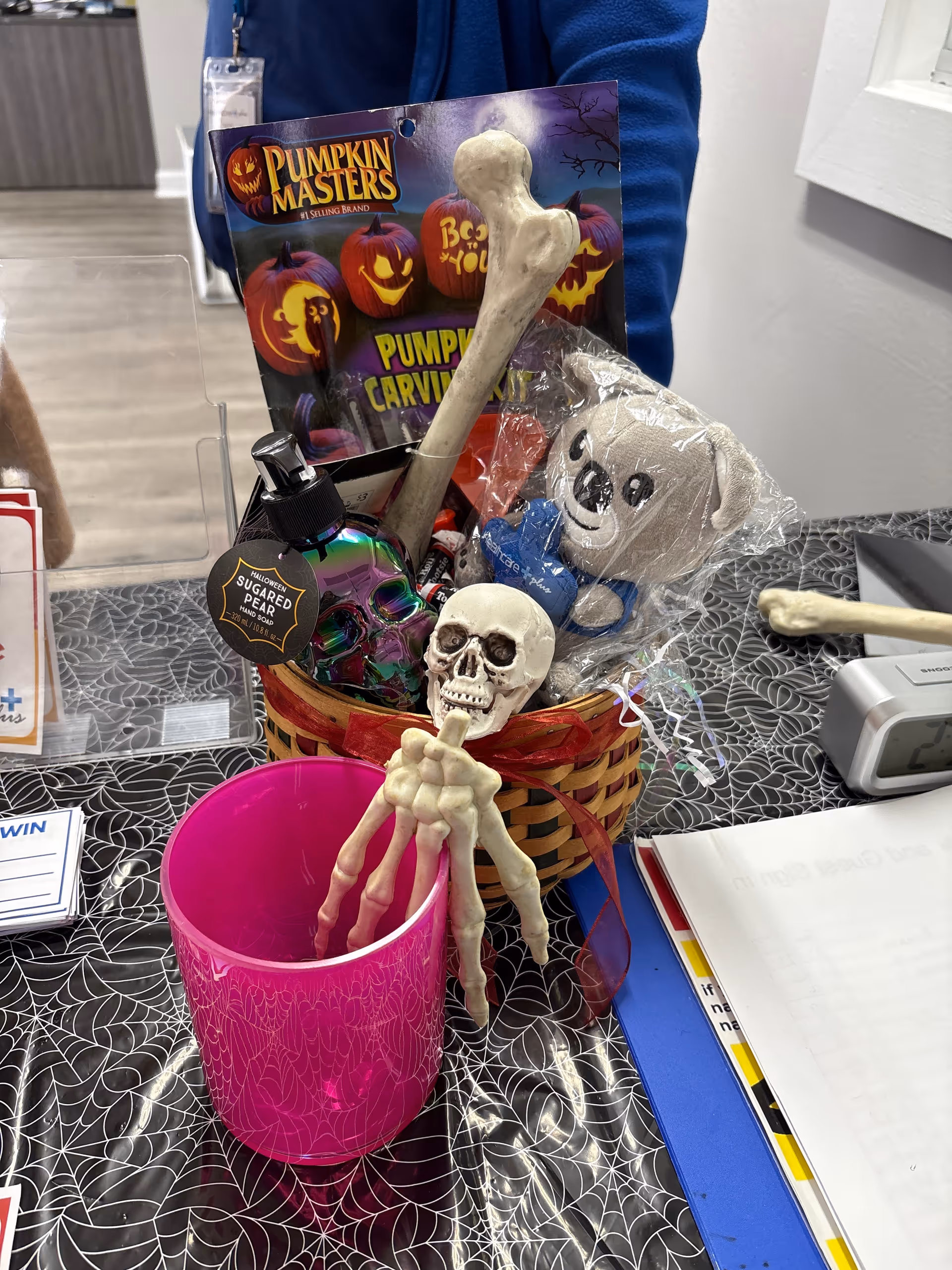 Halloween-themed desk display with skeletons, pumpkins, ghost plush, and a pink cup at a front desk