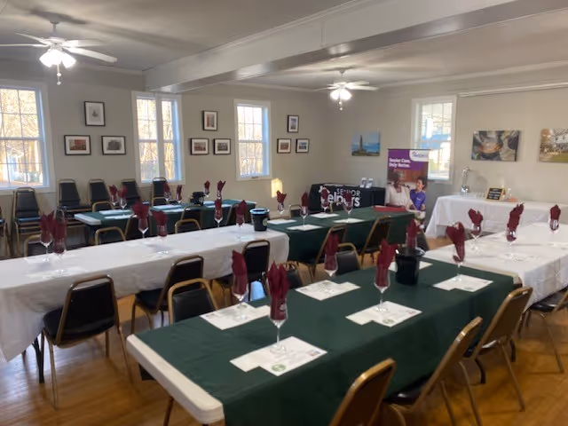Dining room in a seniors facility set for a meal with green tables and red napkins.