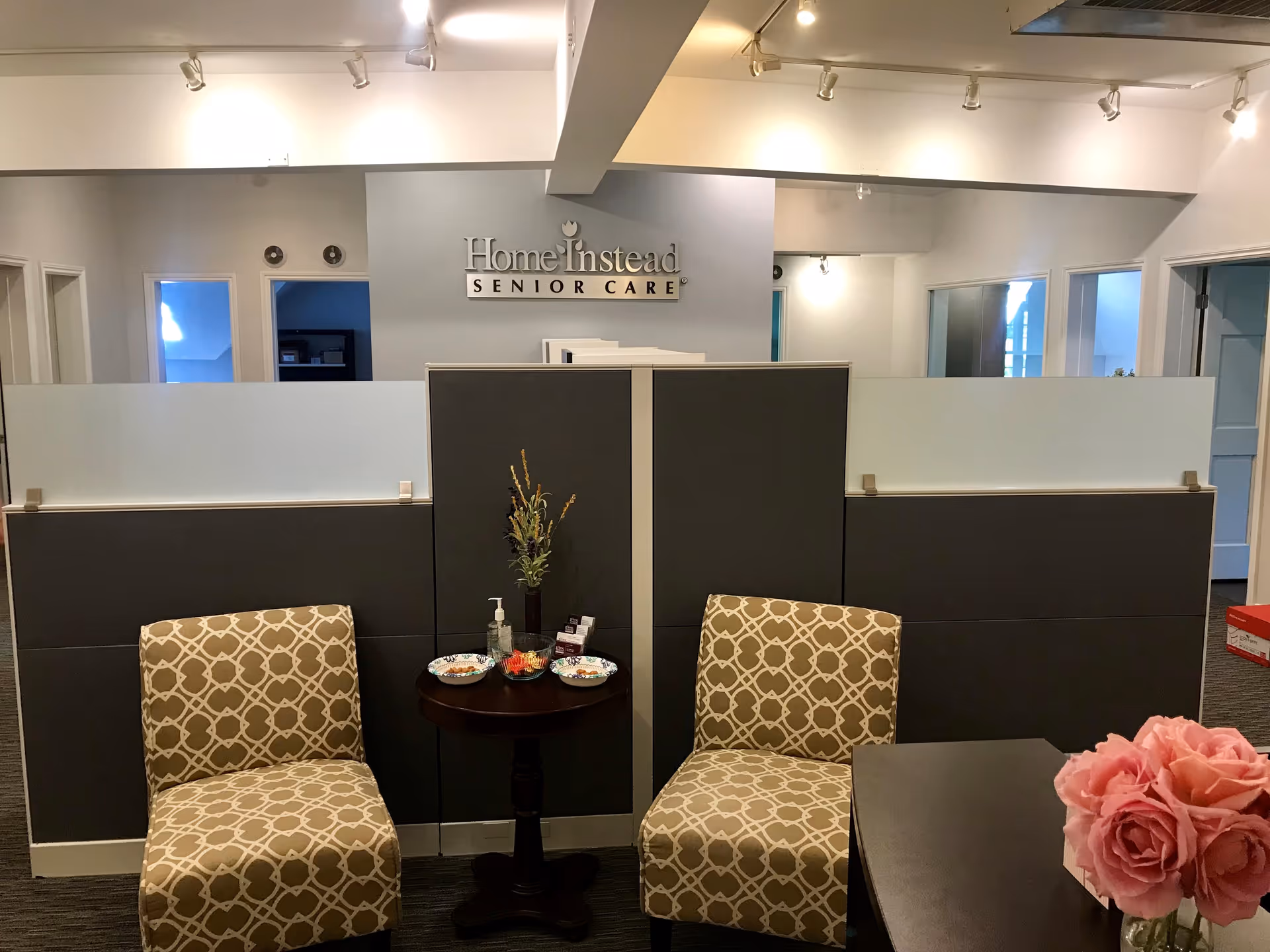 Reception area of Home Instead Senior Care with partitions, chairs, and a flower-adorned table.