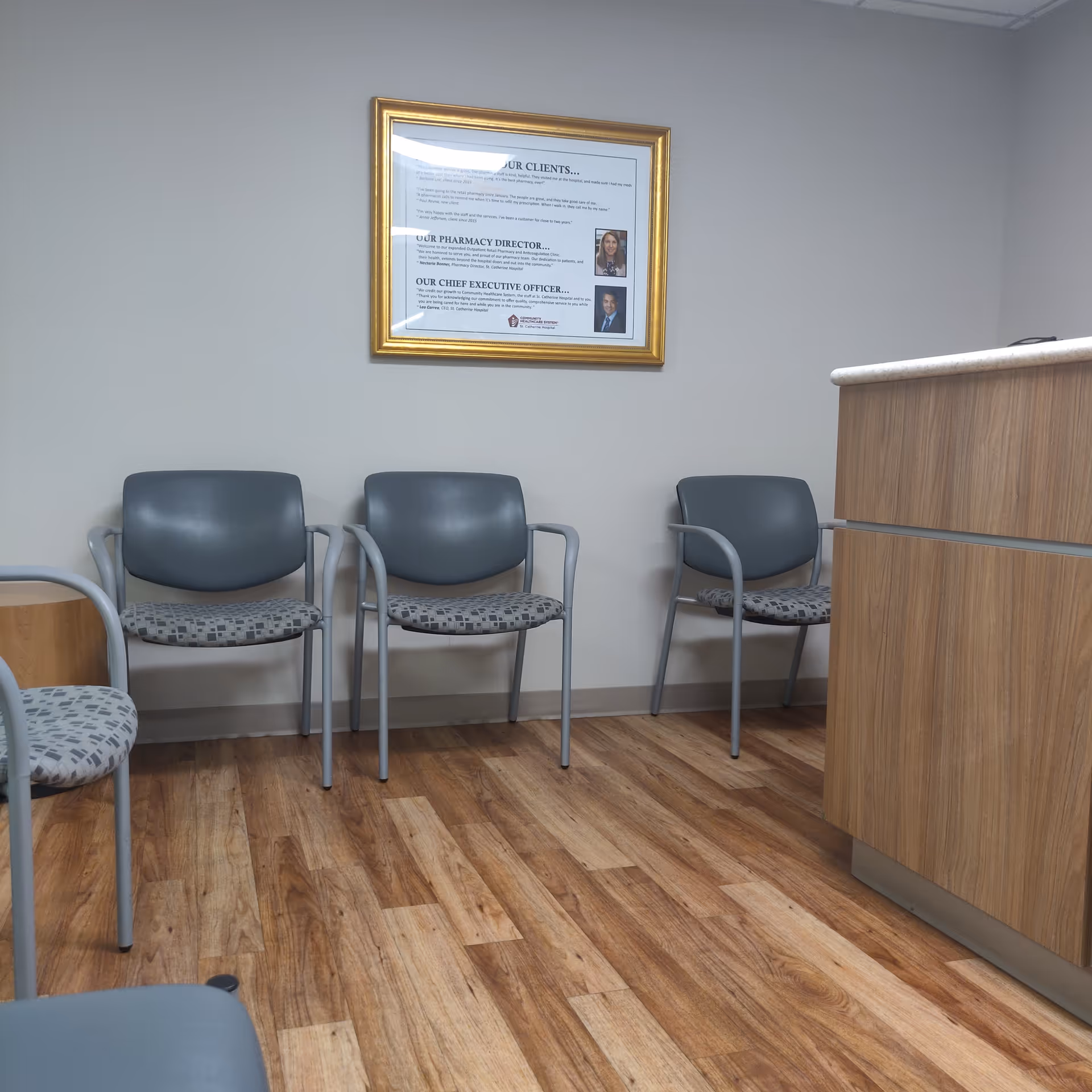Empty waiting area with gray chairs, wood floor, and a framed poster near reception.