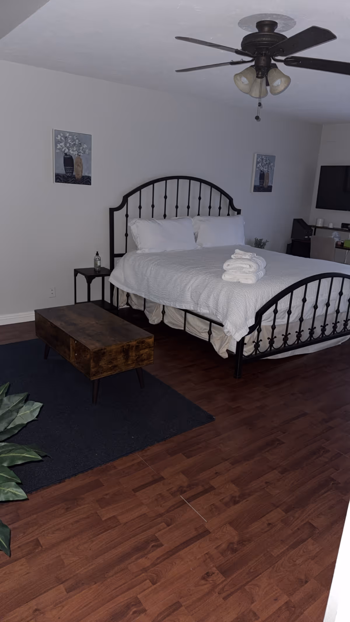 A neatly made bedroom with a metal-framed bed, folded towels, and a ceiling fan.
