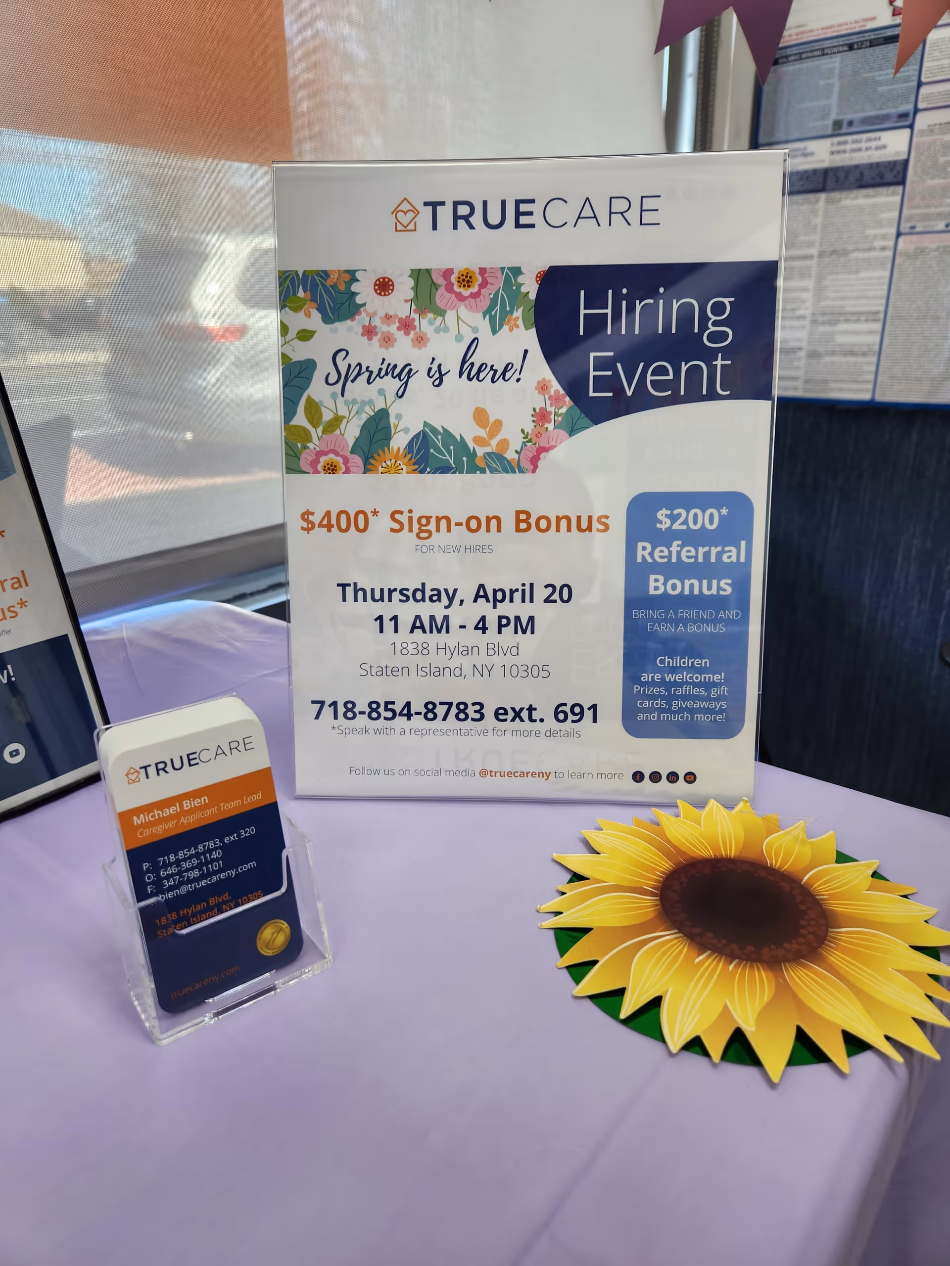 TrueCare Hiring Event sign with floral banner displayed on a purple table.