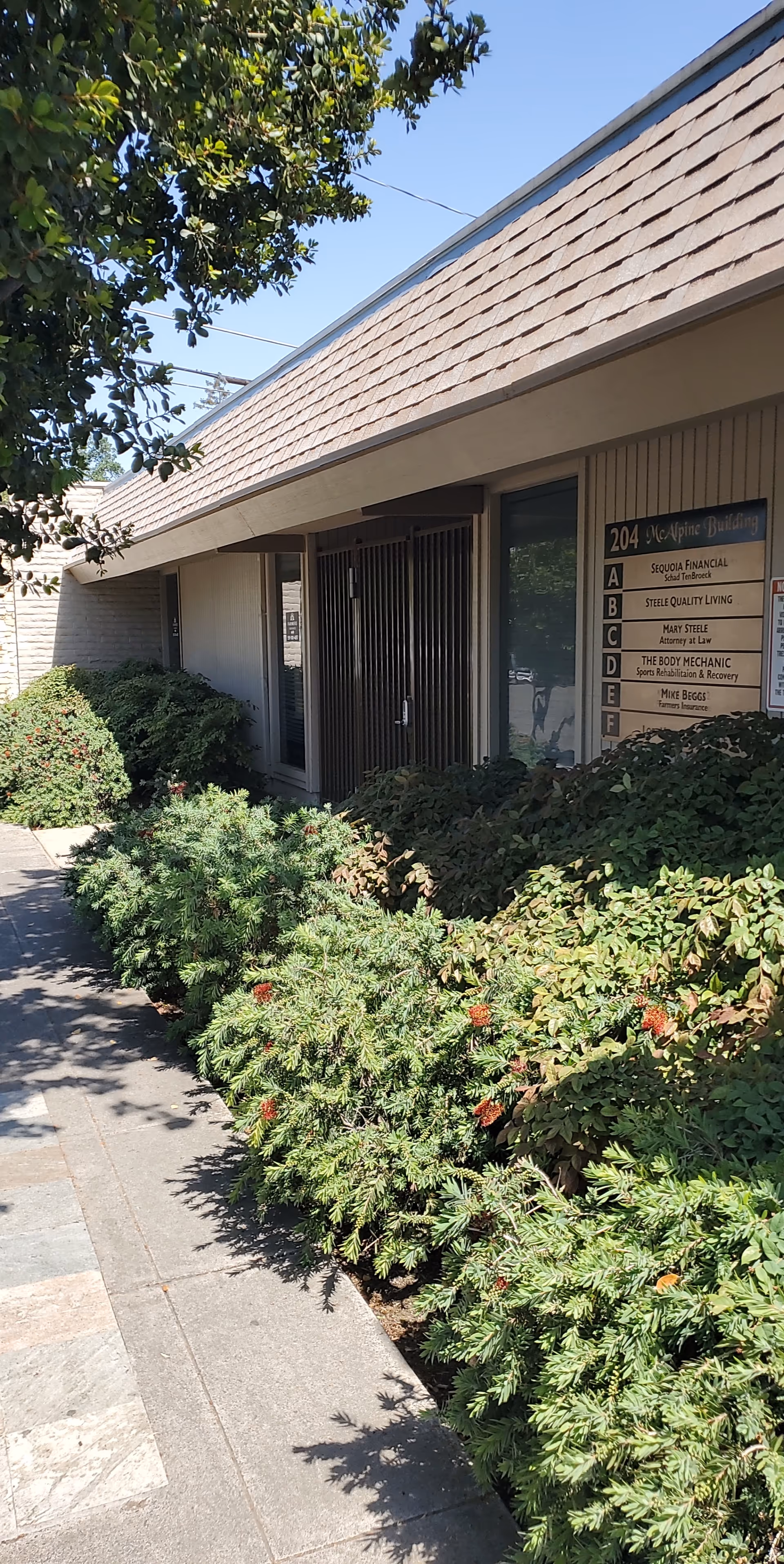 Exterior view of a Senior Helpers building with entrance surrounded by shrubs along a sidewalk.