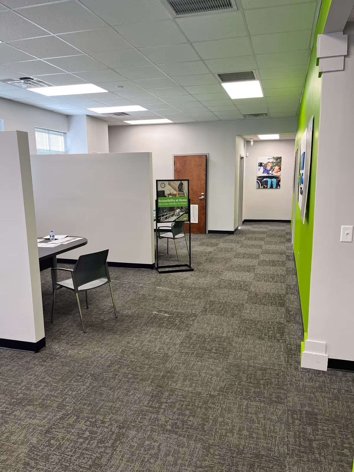 Interior MobilityWorks space with white partitions, a table and chairs, and a bright green wall.
