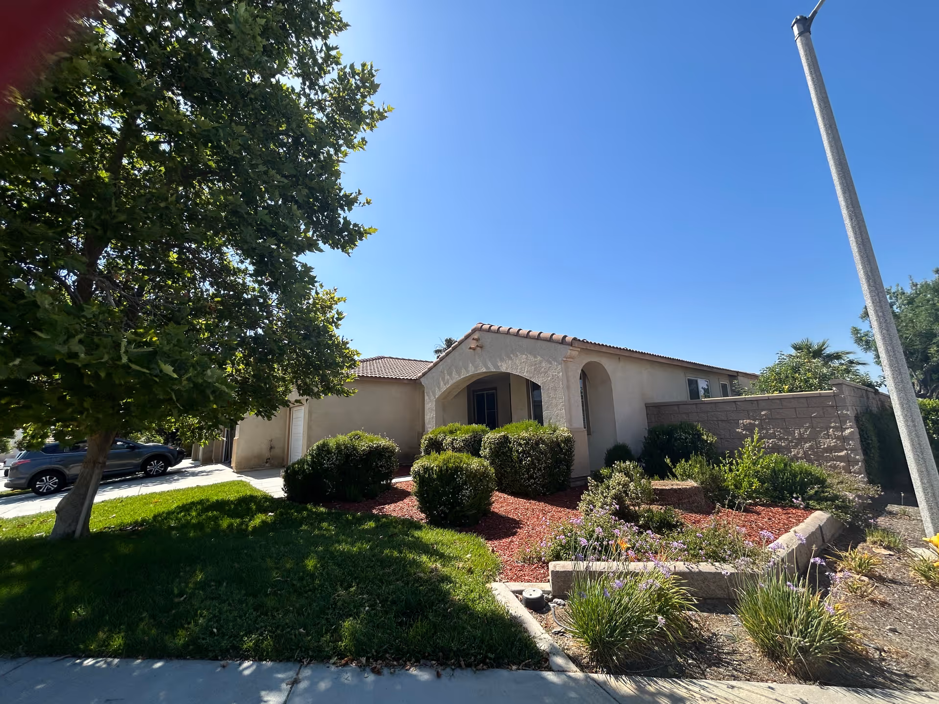 Front view of a single-story beige building with arched entry and landscaped yard