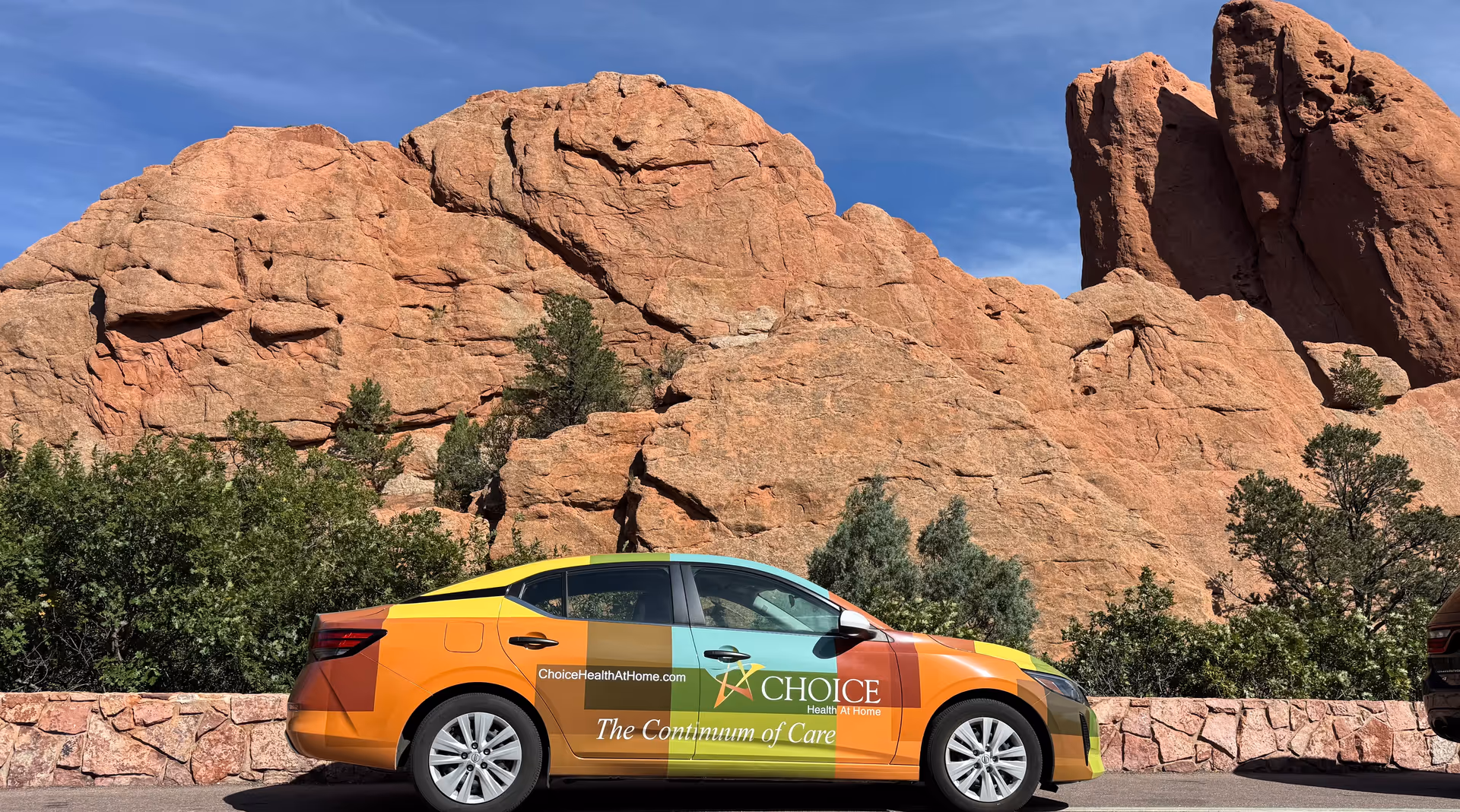 Colorful Choice Health at Home branded car parked beside red rock formations.