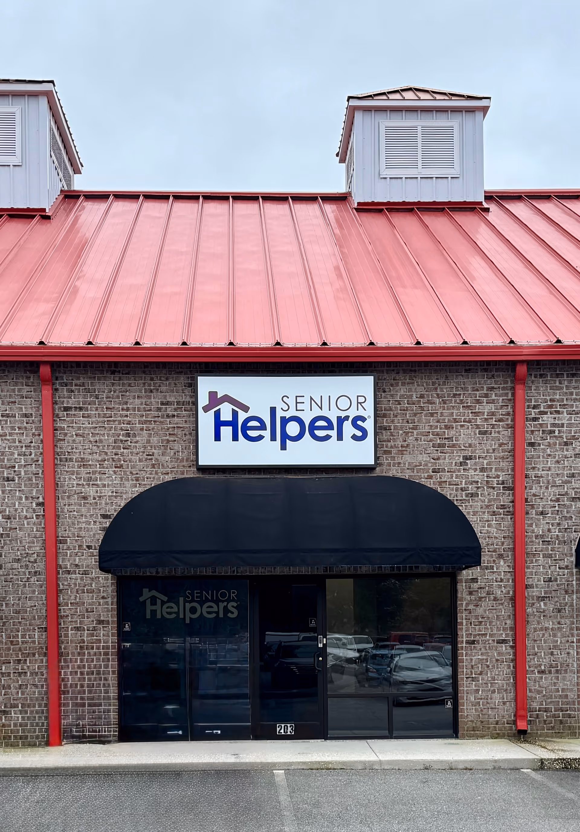Brick building entrance with Senior Helpers sign, black canopy, and red metal roof.