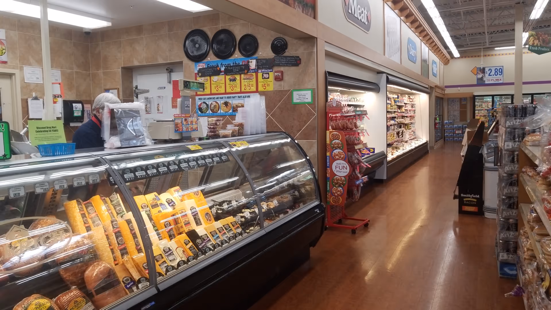 Inside a Discount Drug Mart, a curved deli counter displays meats and cheeses.
